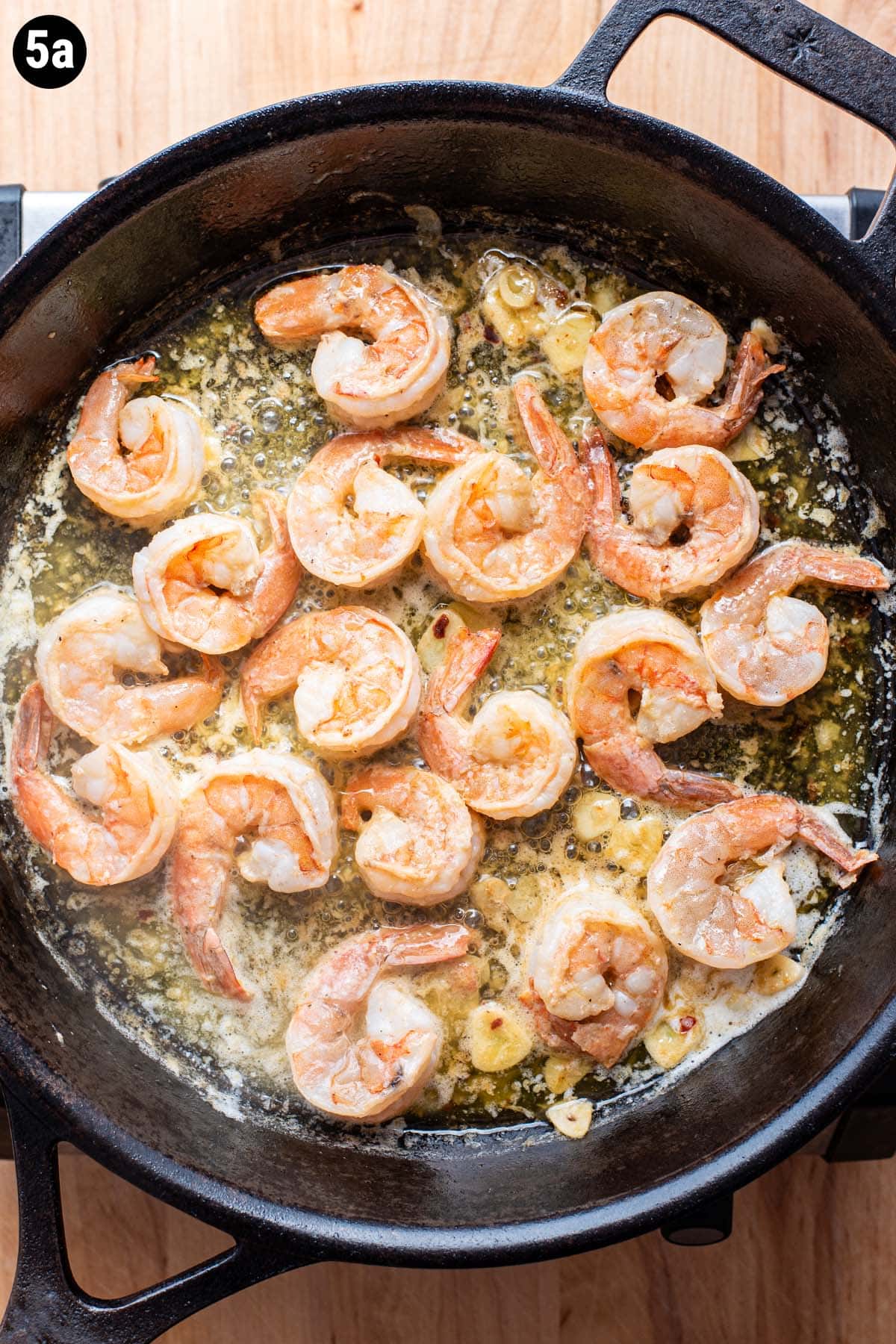 Shrimp simmering in a cast iron skillet with butter, lemon, garlic, and wine.