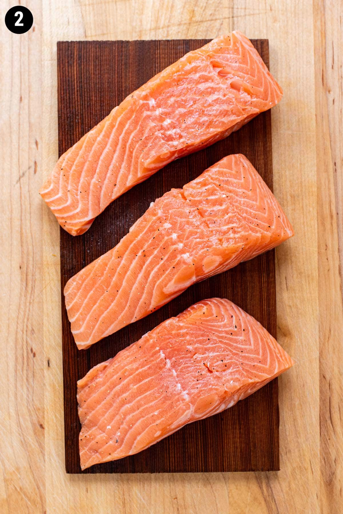 Raw, uncooked salmon filets on a cedar plank before grilling.