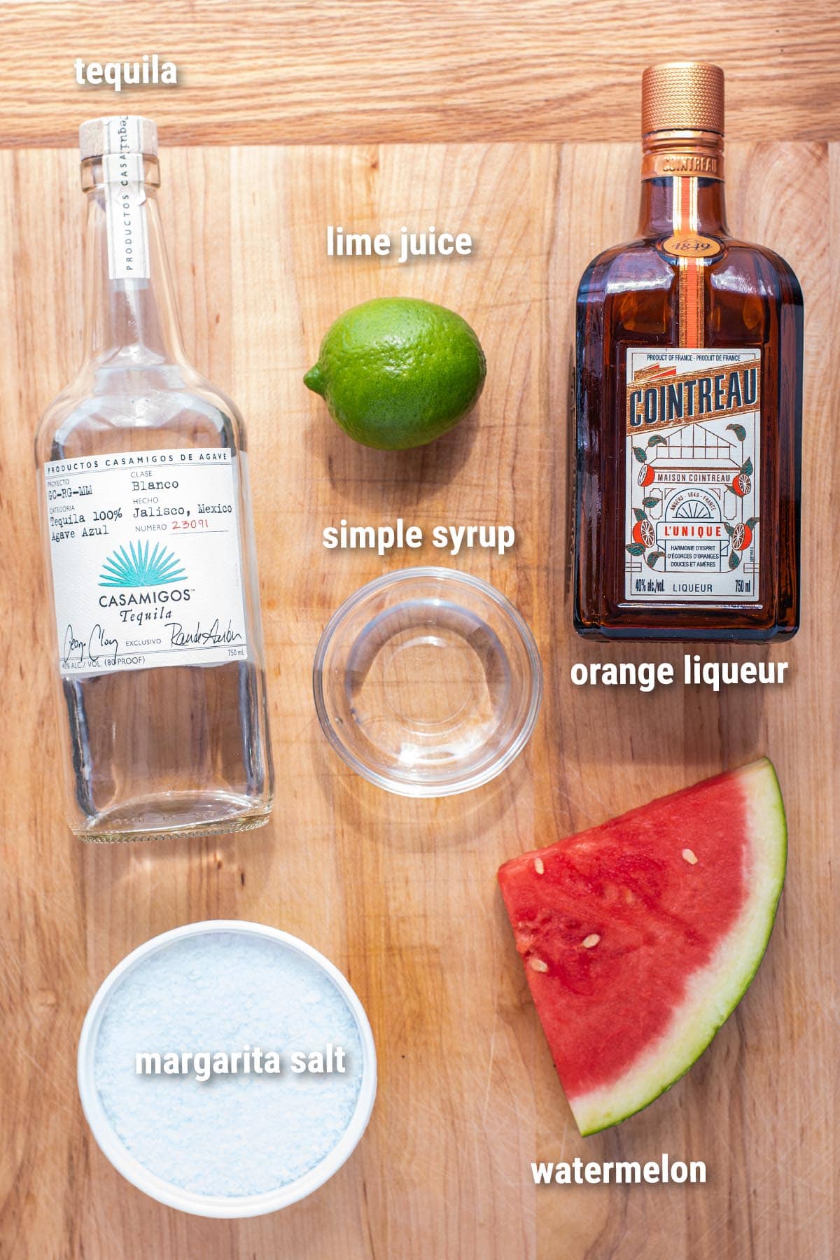 Watermelon margarita ingredients laid out on a wooden cutting board.