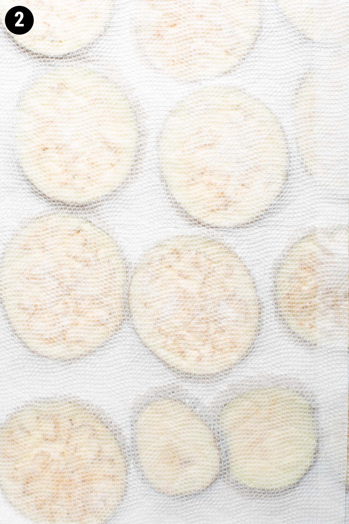 Thinly sliced eggplant covered top and bottom with paper towel to absorb moisture.