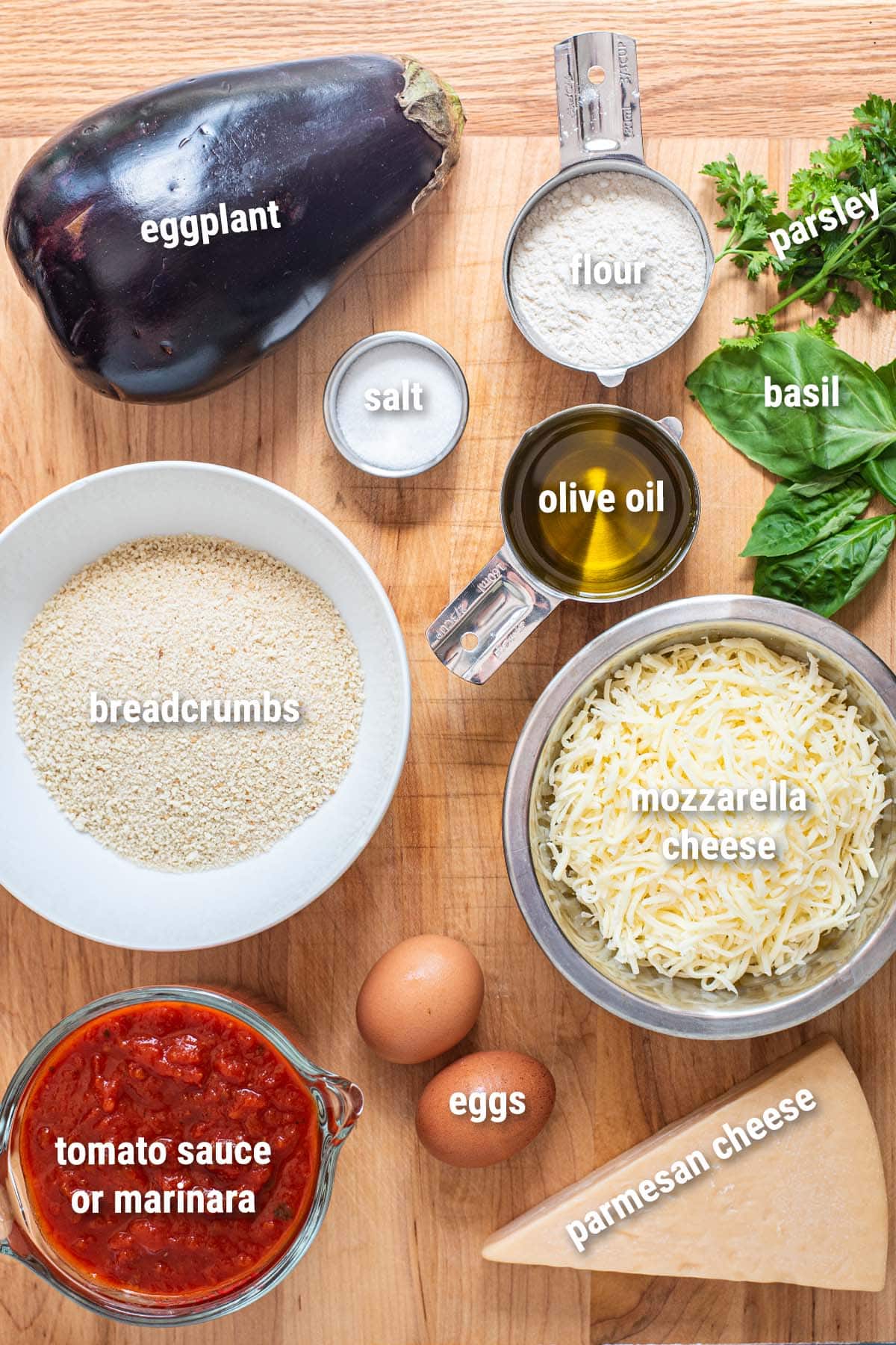 Raw, uncooked eggplant parmesan ingredients laid out on a wooden cutting board.