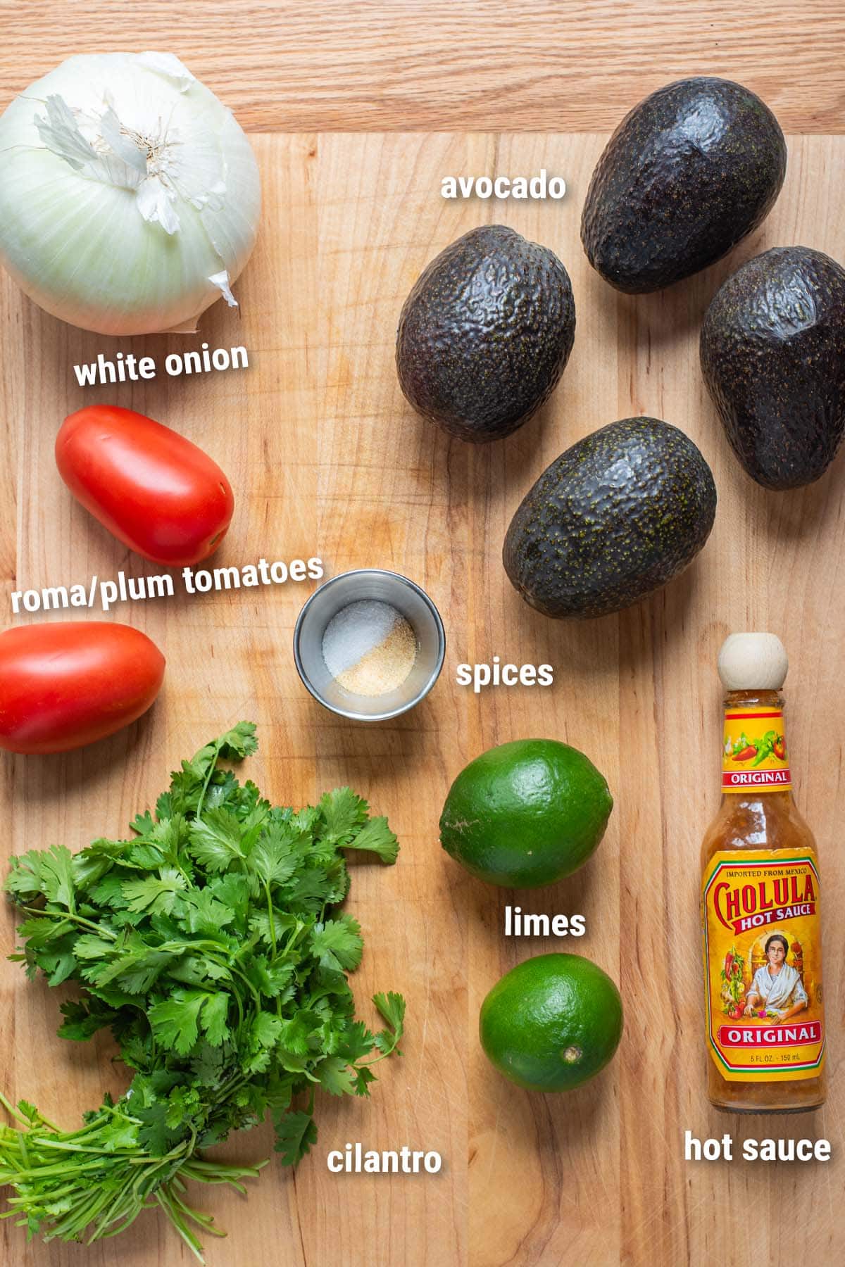 Guacamole ingredient laid out on a wooden cutting board.