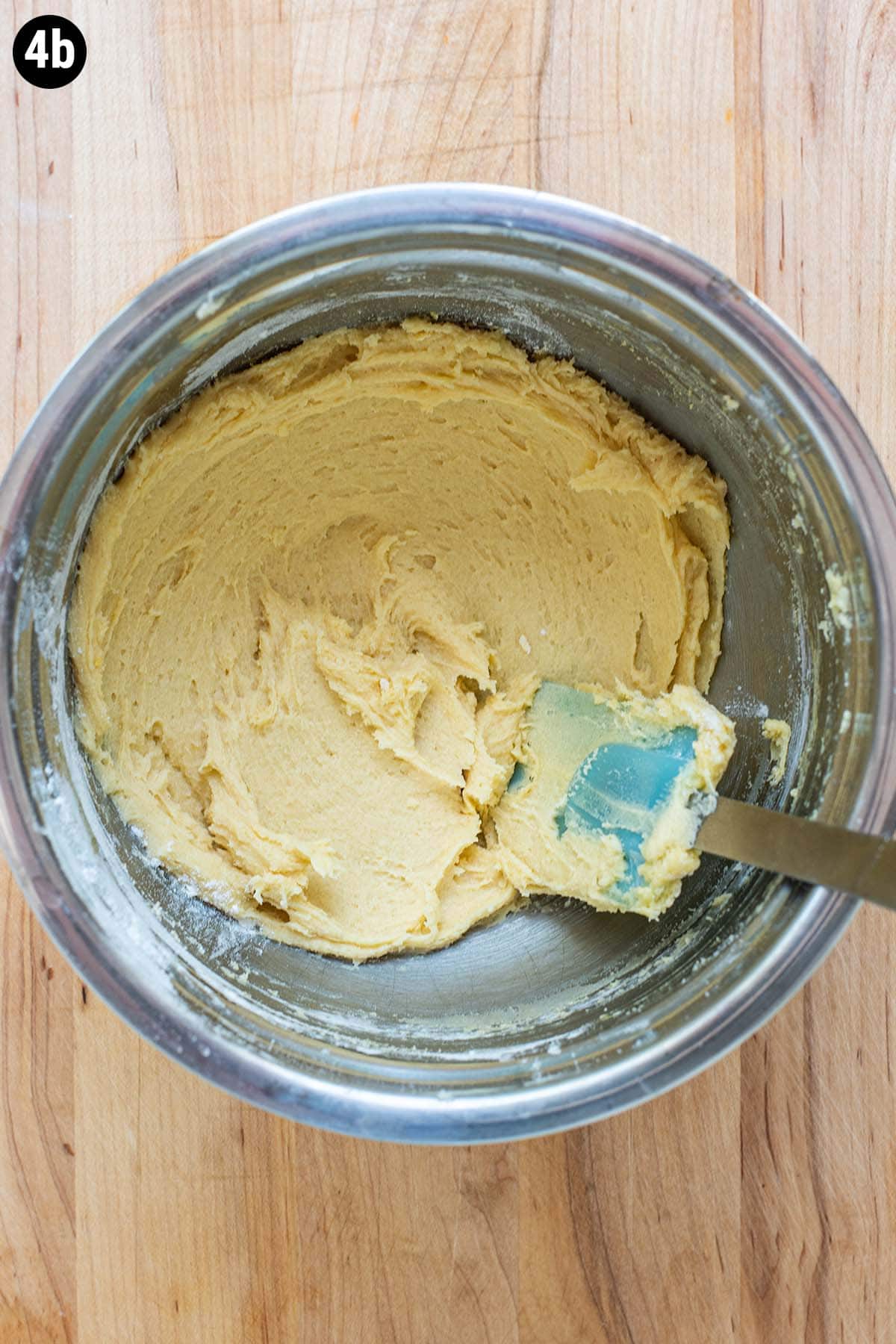 A simple thick batter of sugar, butter, flour, and egg in a stainless steel bowl.