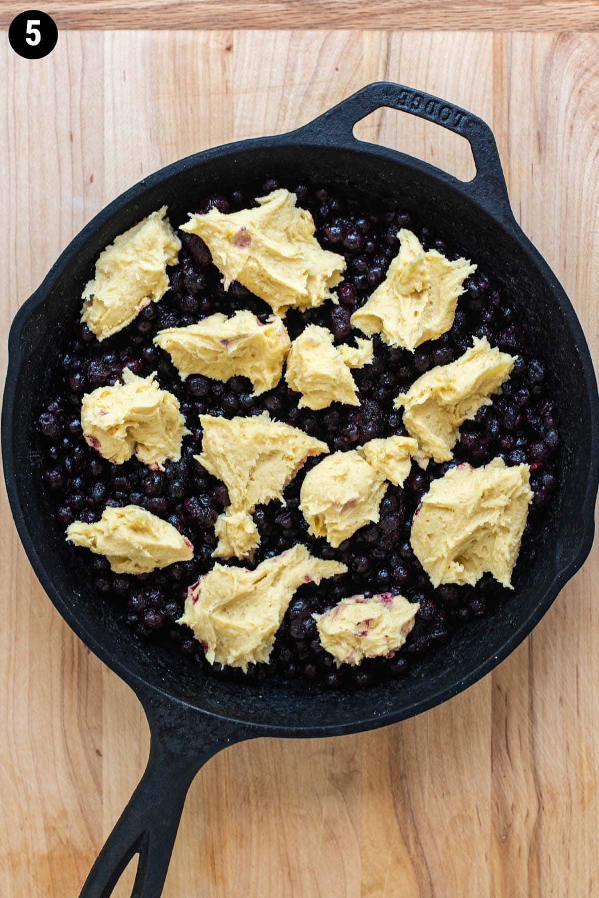 Unbaked blueberry cobbler in a cast iron skillet topped with dough balls of batter.