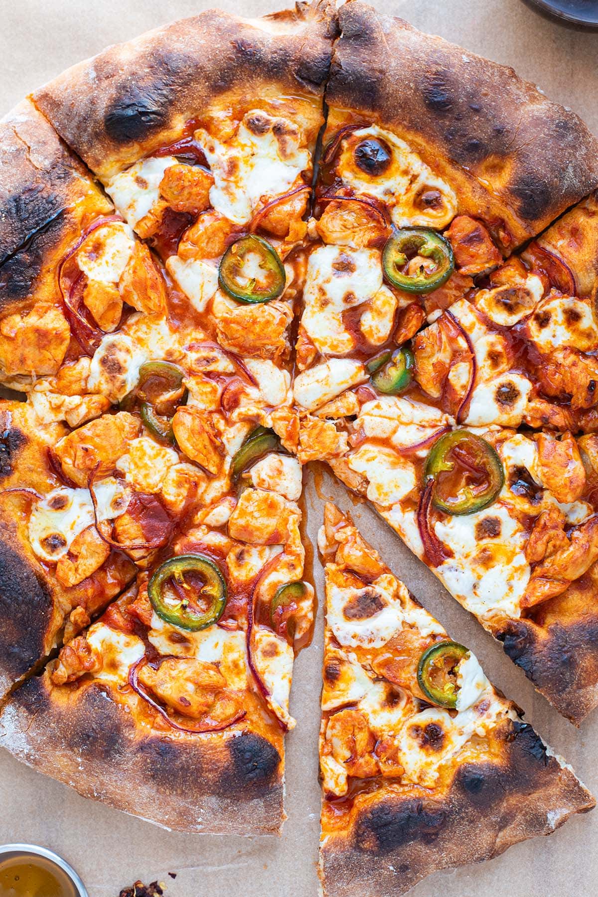 A buffalo chicken pizza with golden charred crust topped with fresh jalapeno, fresh mozzarella, red onion, and chicken.