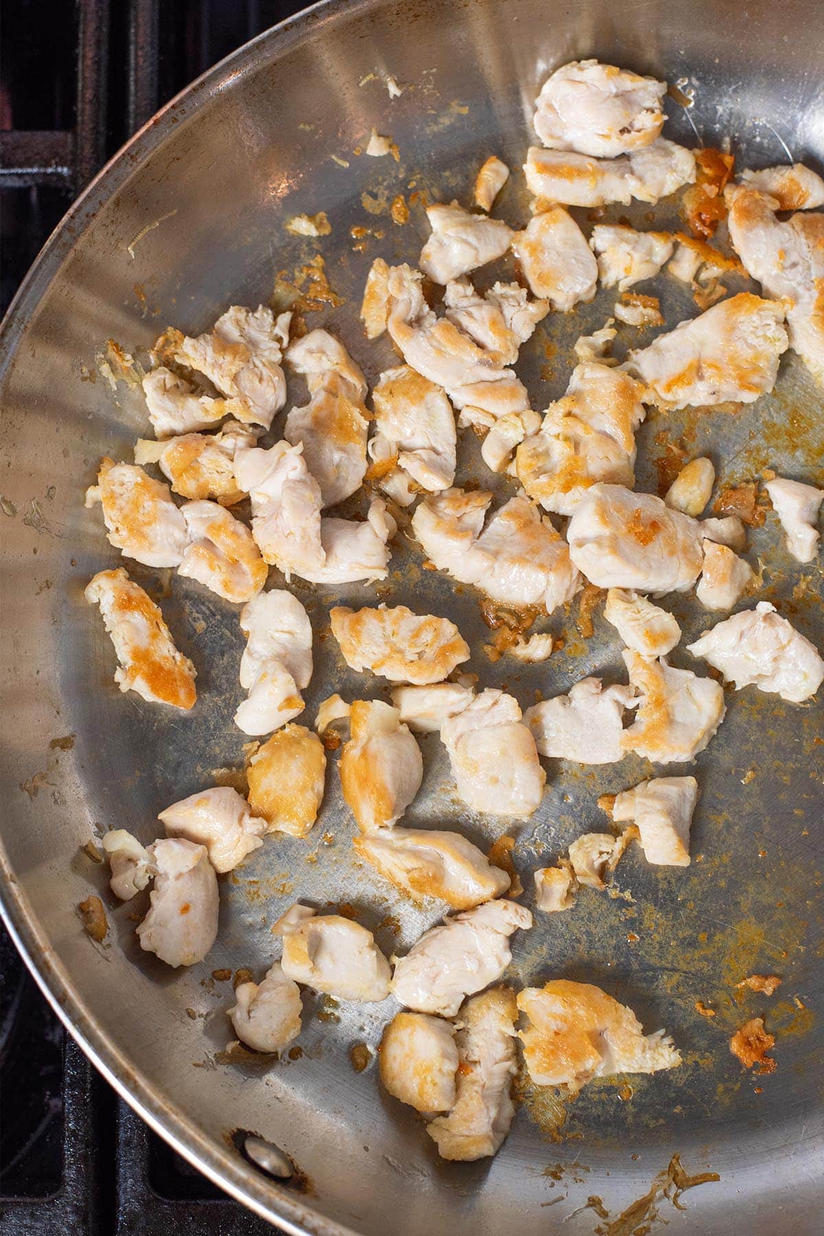 Chopped chicken tenders in a stainless steel pan with a golden exterior.