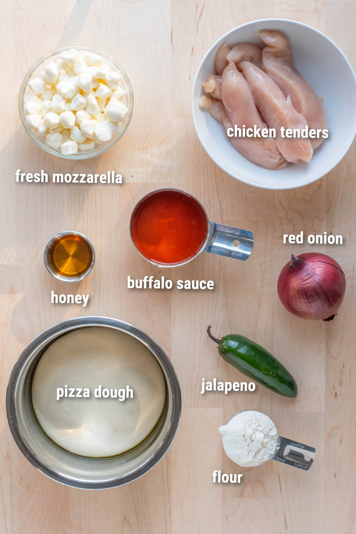 Raw, uncooked buffalo chicken pizza ingredients laid out on a wooden cutting board.
