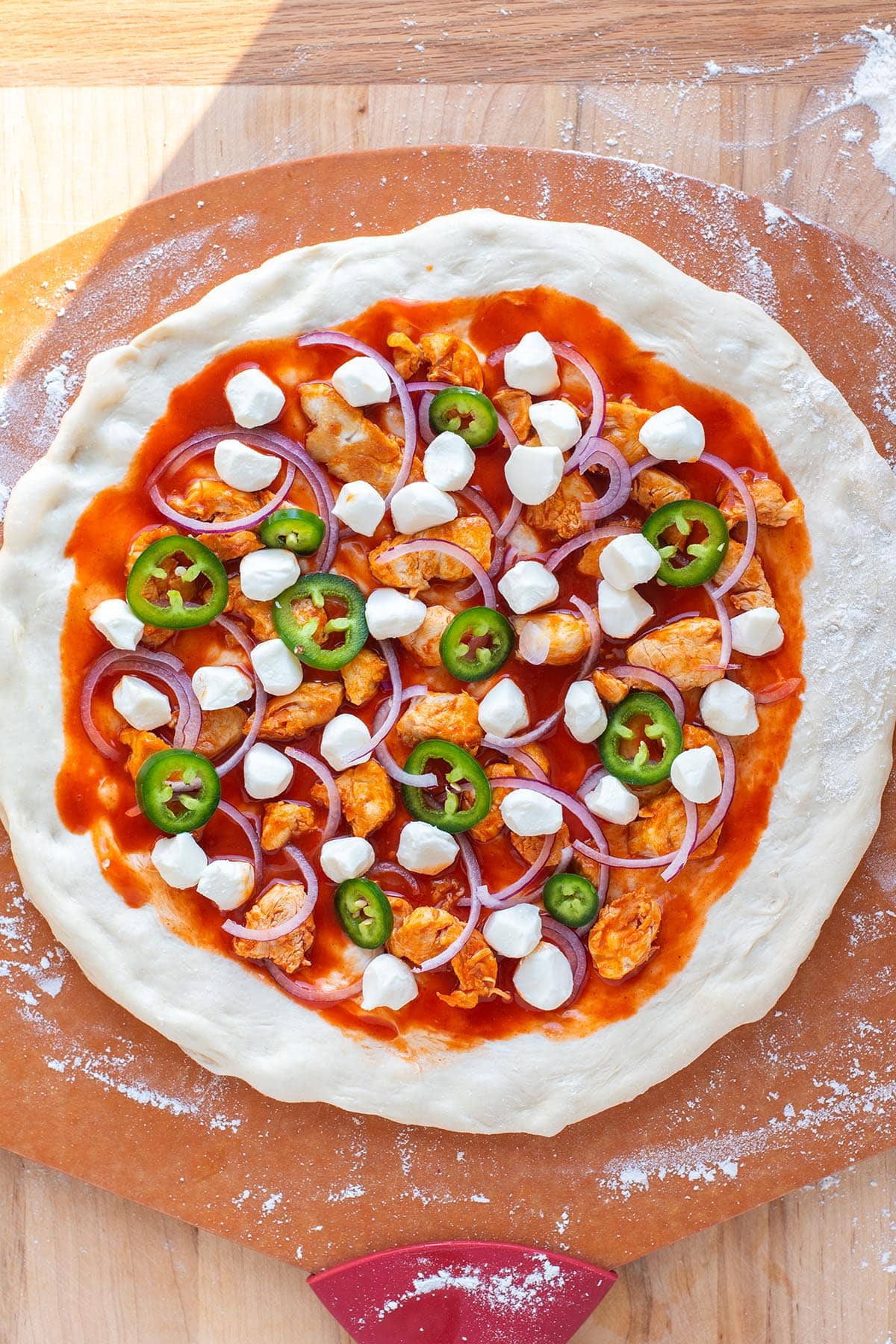 Unbaked buffalo chicken pizza on a pizza peel with toppings.