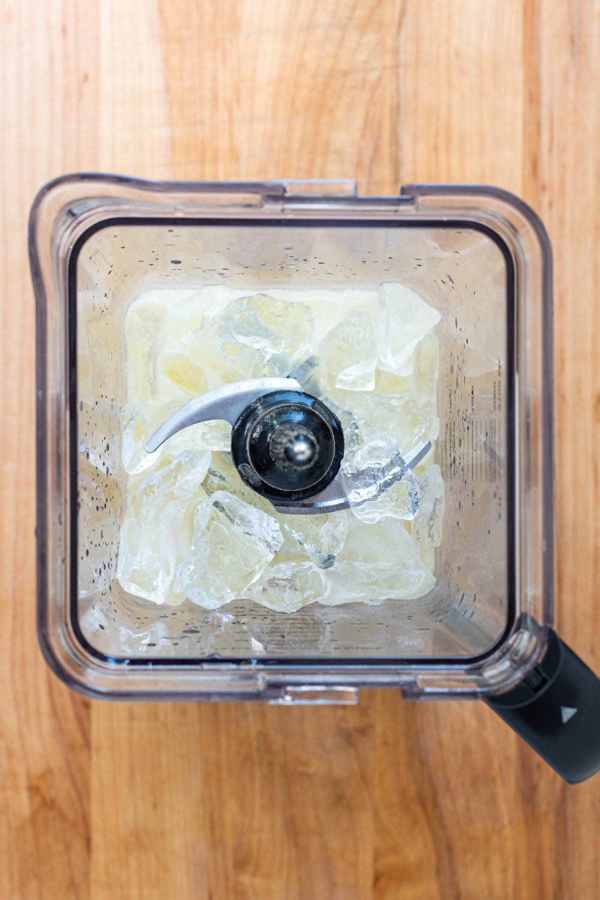 A top down view of a blender filled with cream of coconut, ice, rum, and pineapple juice.
