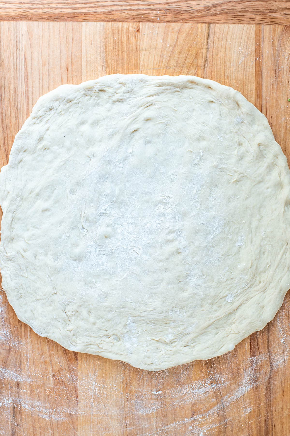 A pizza crust on a floured wooden surface.