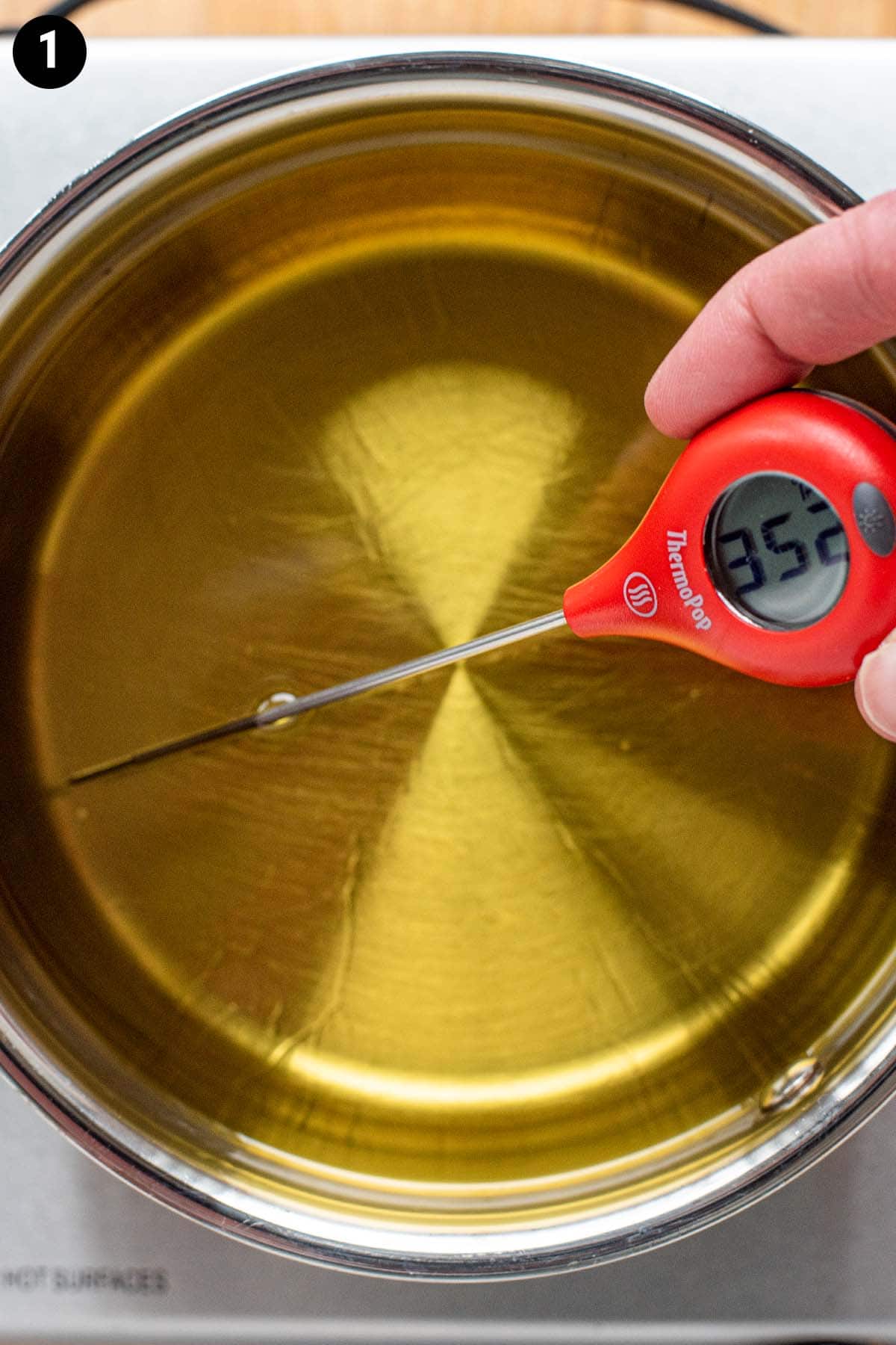 Canola oil measuring 350 degrees Fahrenheit with a digital thermometer in a small saucepan.