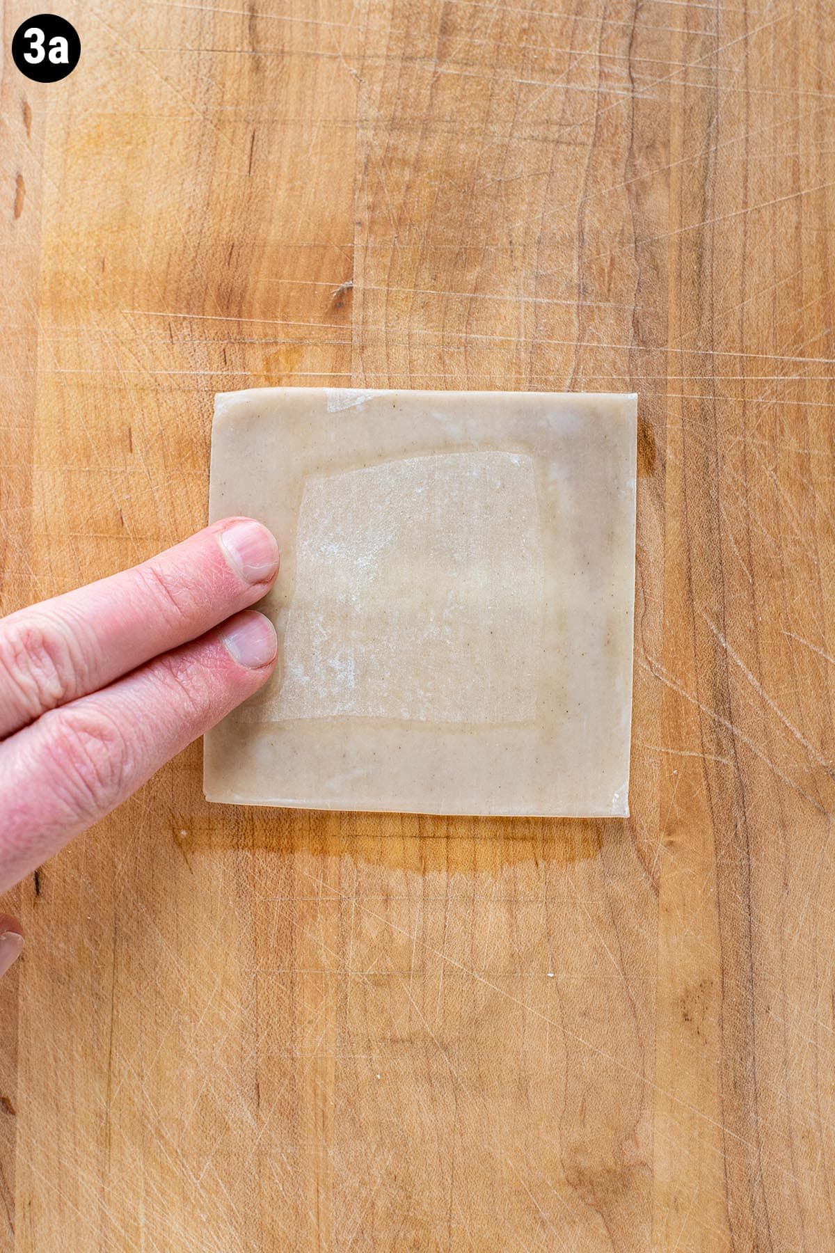 Two fingers wetting the edges of a wonton wrapper with water.