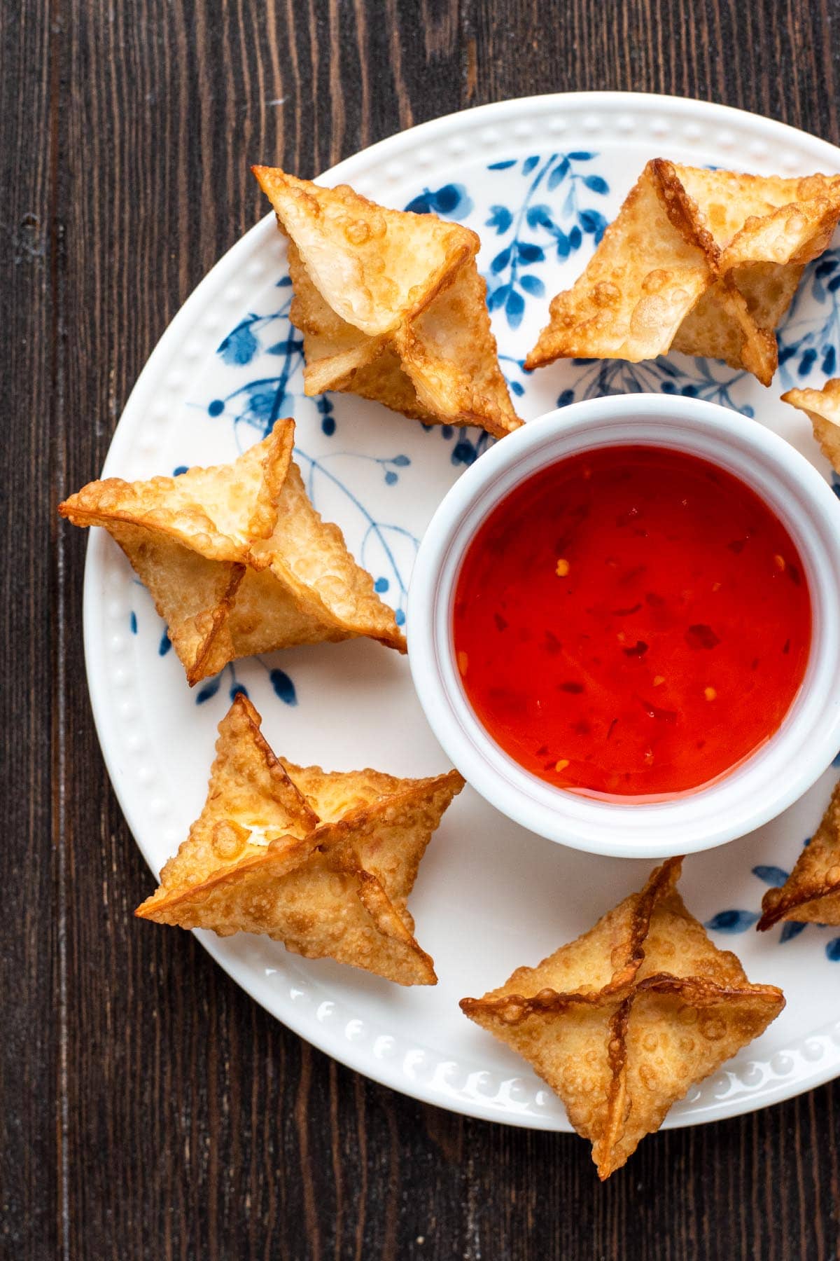 Crispy golden fried crab rangoons on a white plate served with sweet chili sauce.