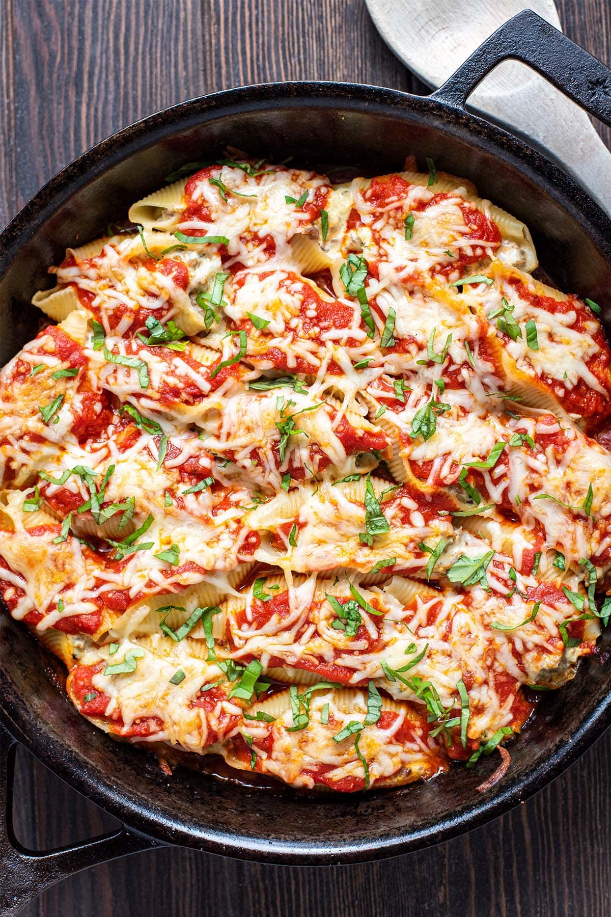 Golden baked sausage and ricotta stuffed shells in a cast iron skillet topped with fresh basil.