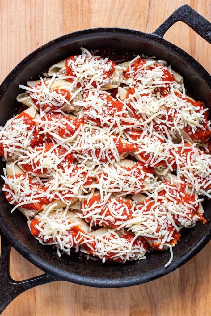 Unbaked ricotta stuffed shells topped with marinara and shredded mozzarella cheese.