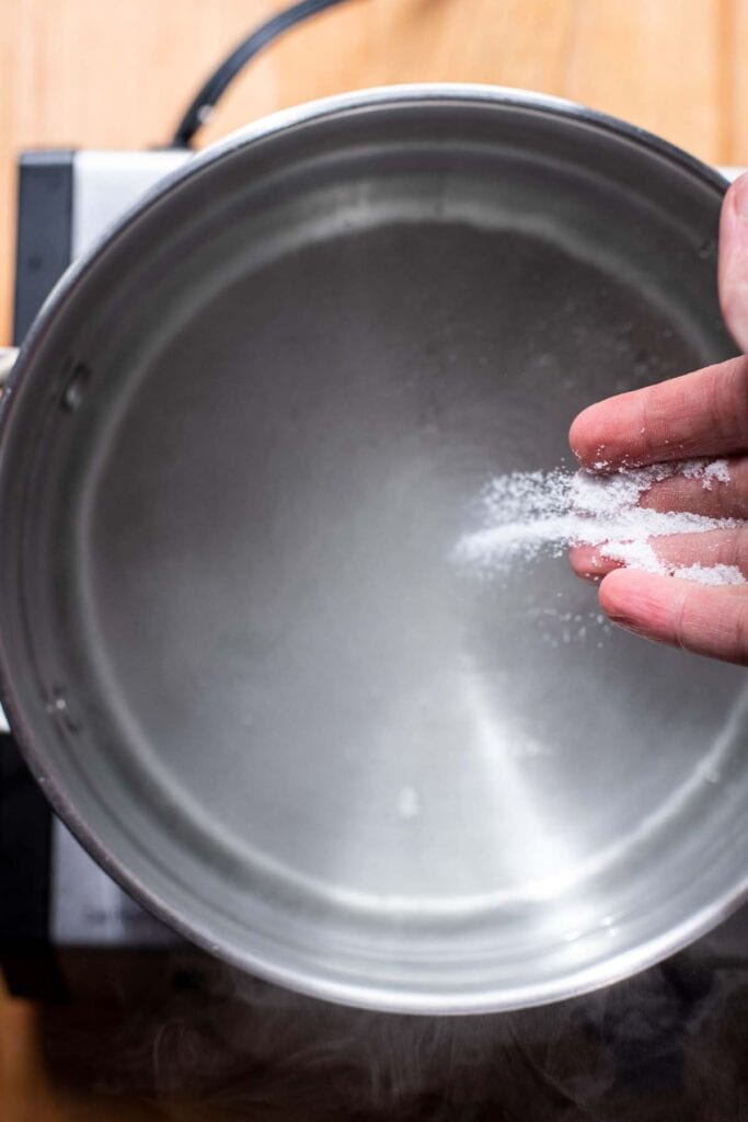 A hand adding salt to simmering pasta water.
