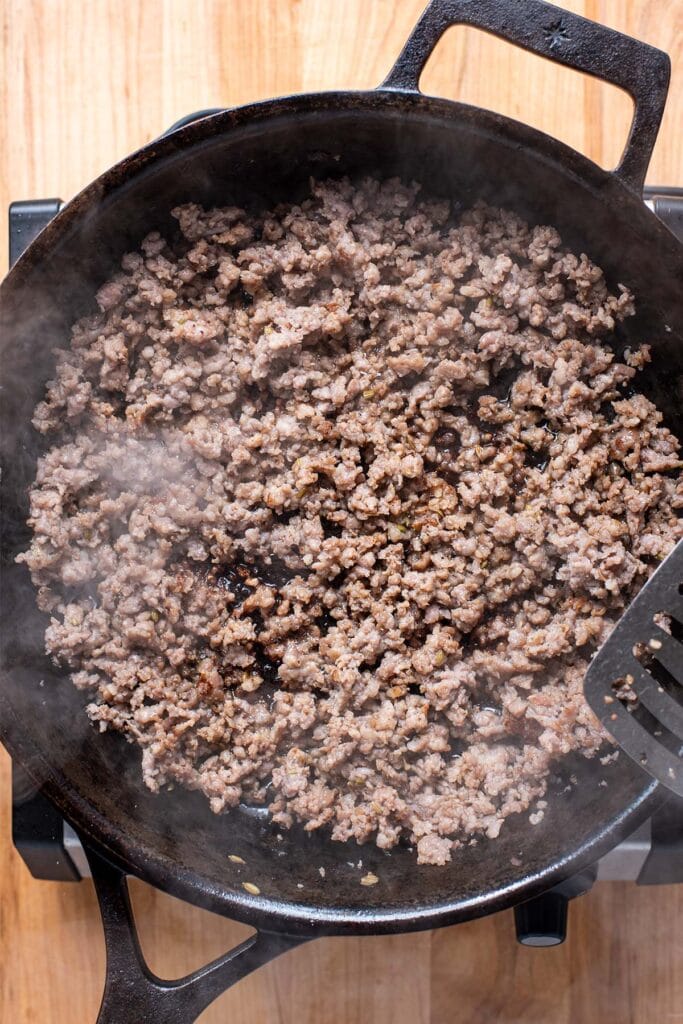 Fully cooked and browned sausage cooking in a cast iron skillet.