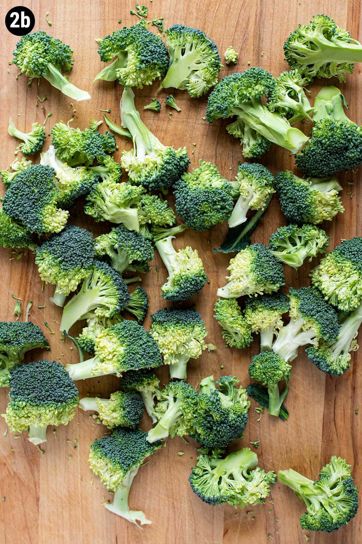 Raw broccoli florets separated into small florets on a wooden cutting board.