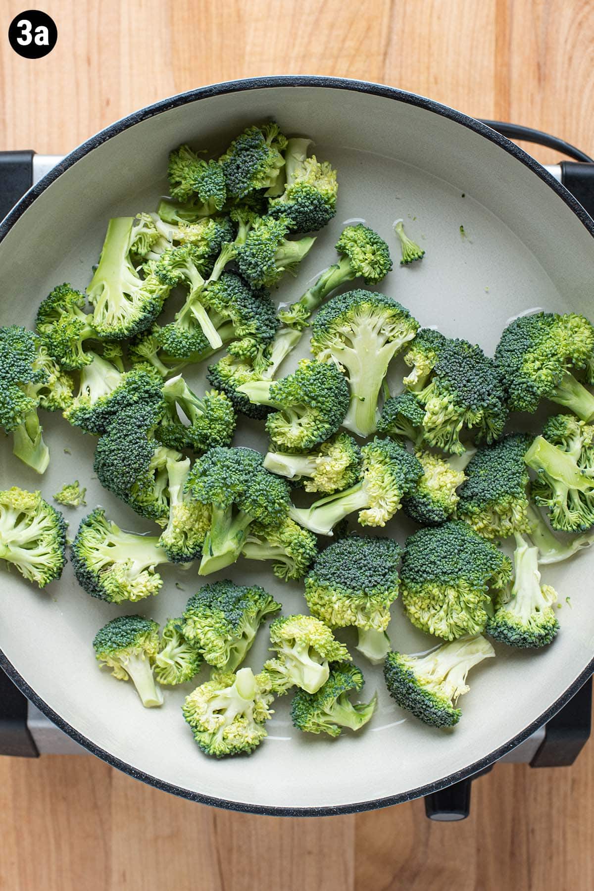 Raw broccoli florets in a shallow pan with water.