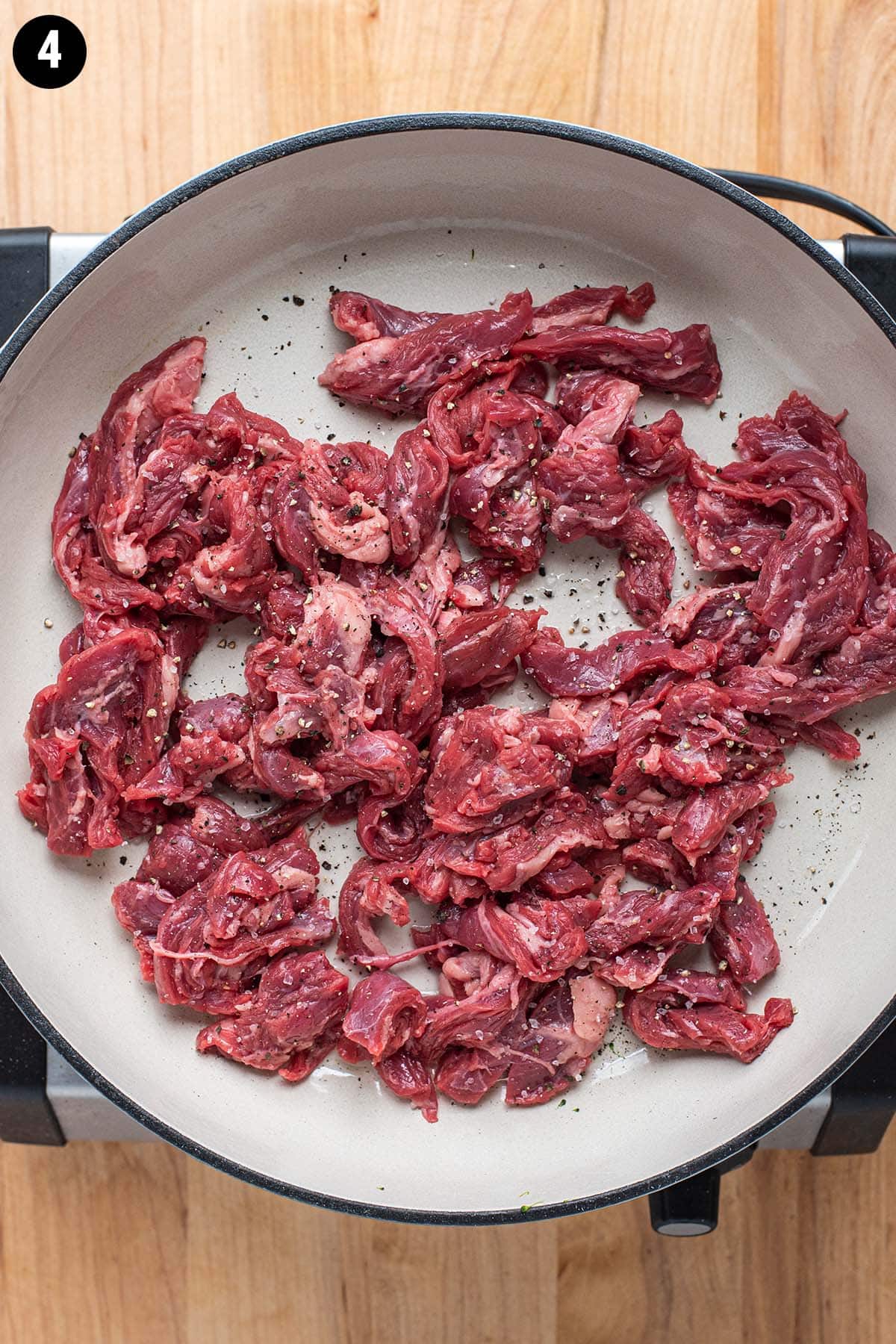 Raw flank steak seasoned with salt and pepper starting to cook in a enameled cast iron pan.
