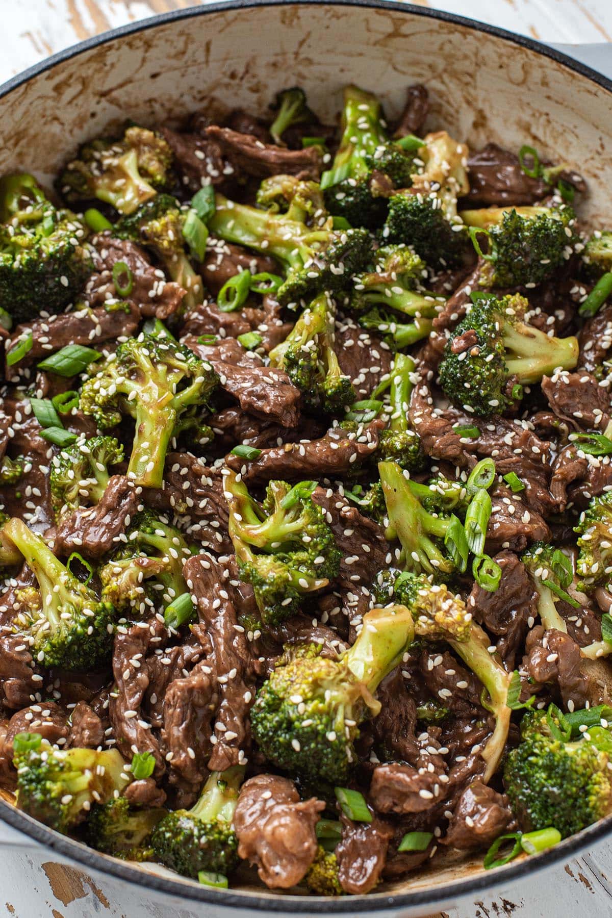 Finished savory beef and broccoli in a cast iron skillet topped with sesame seeds and green onion.