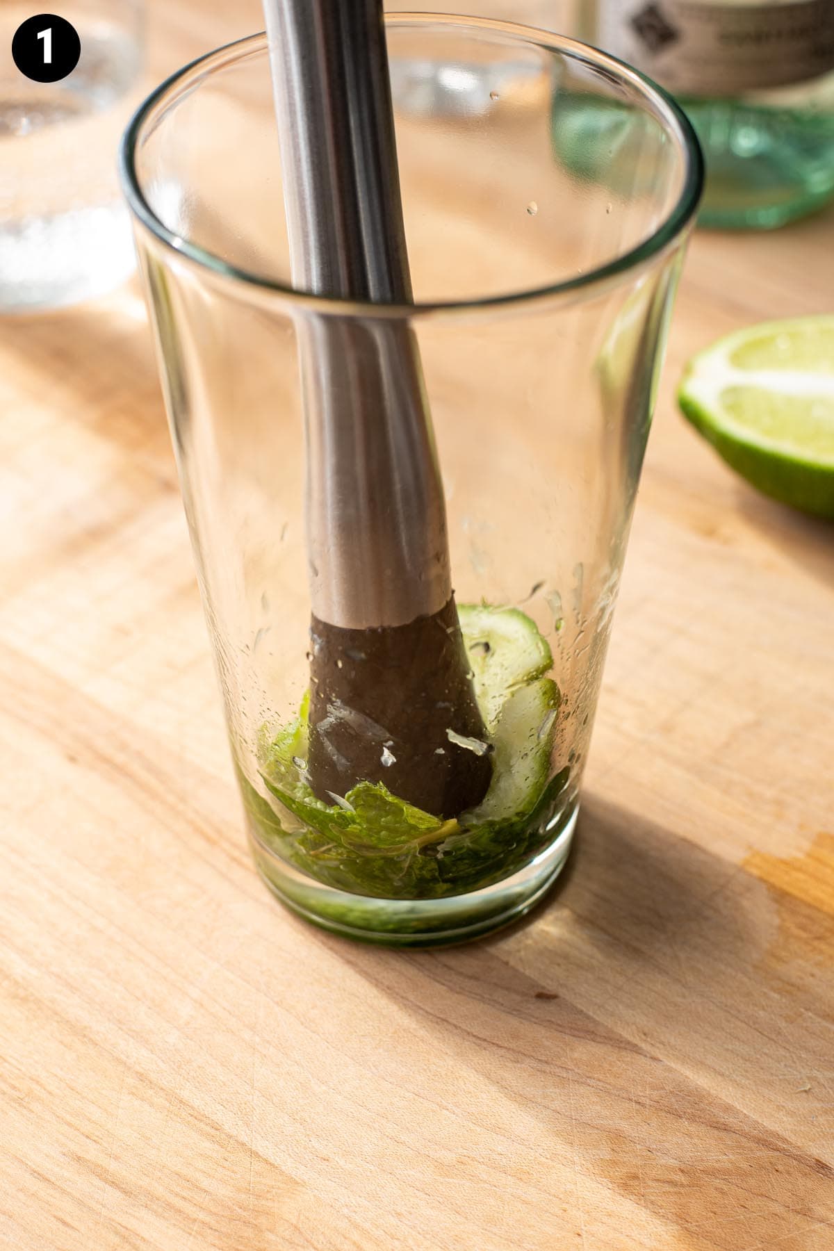 A stainless muddler muddling mint leaves and limes wedges in a cocktail shaker.