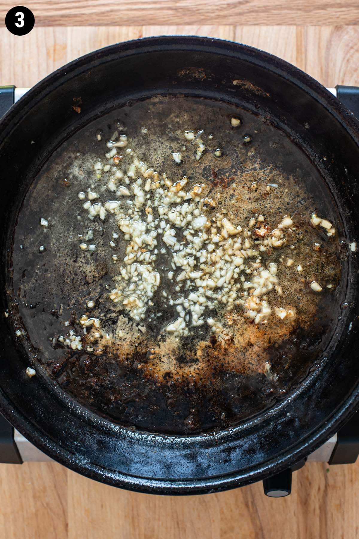 Minced garlic simmering sin a cast iron skillet with lemon, oil, and butter.