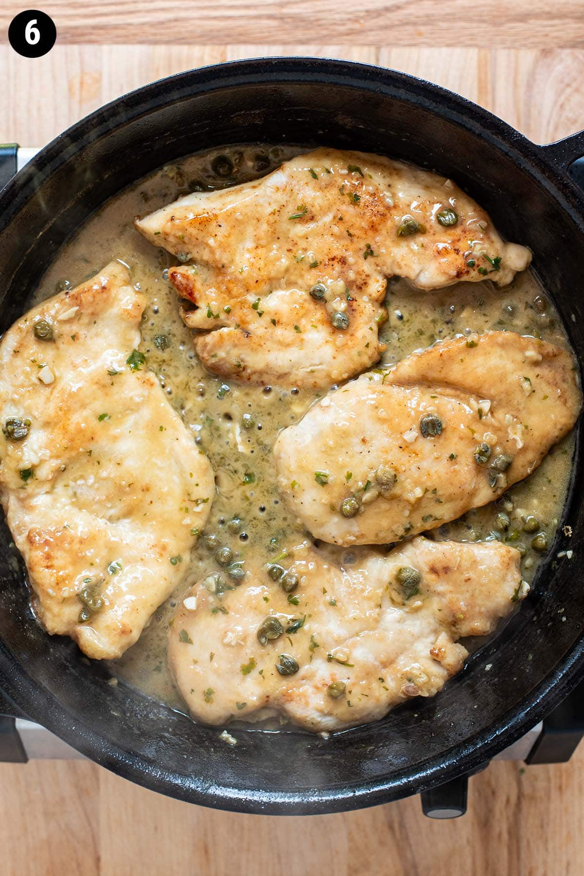 Chicken piccata simmering in a cast iron skillet.