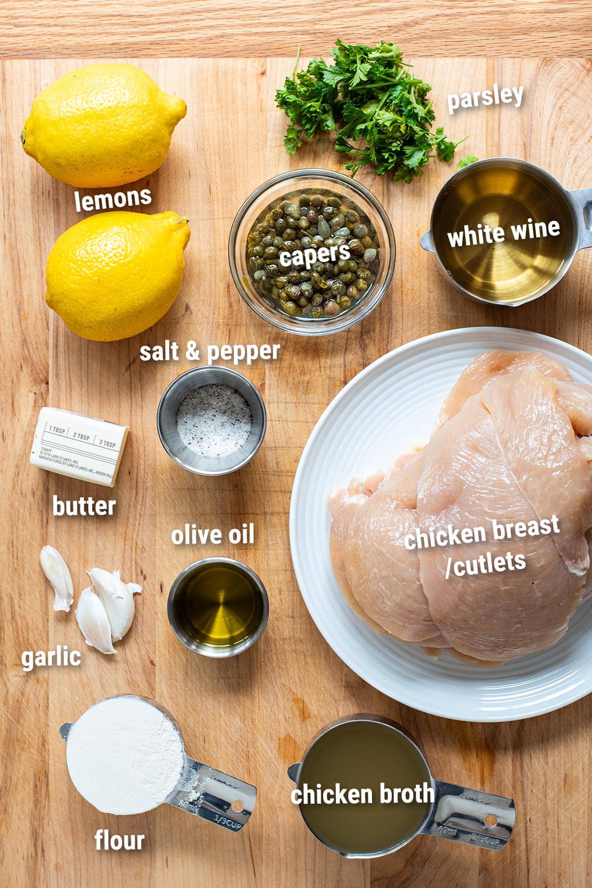 Raw, uncooked chicken piccata ingredients laid out on a wooden cutting board.