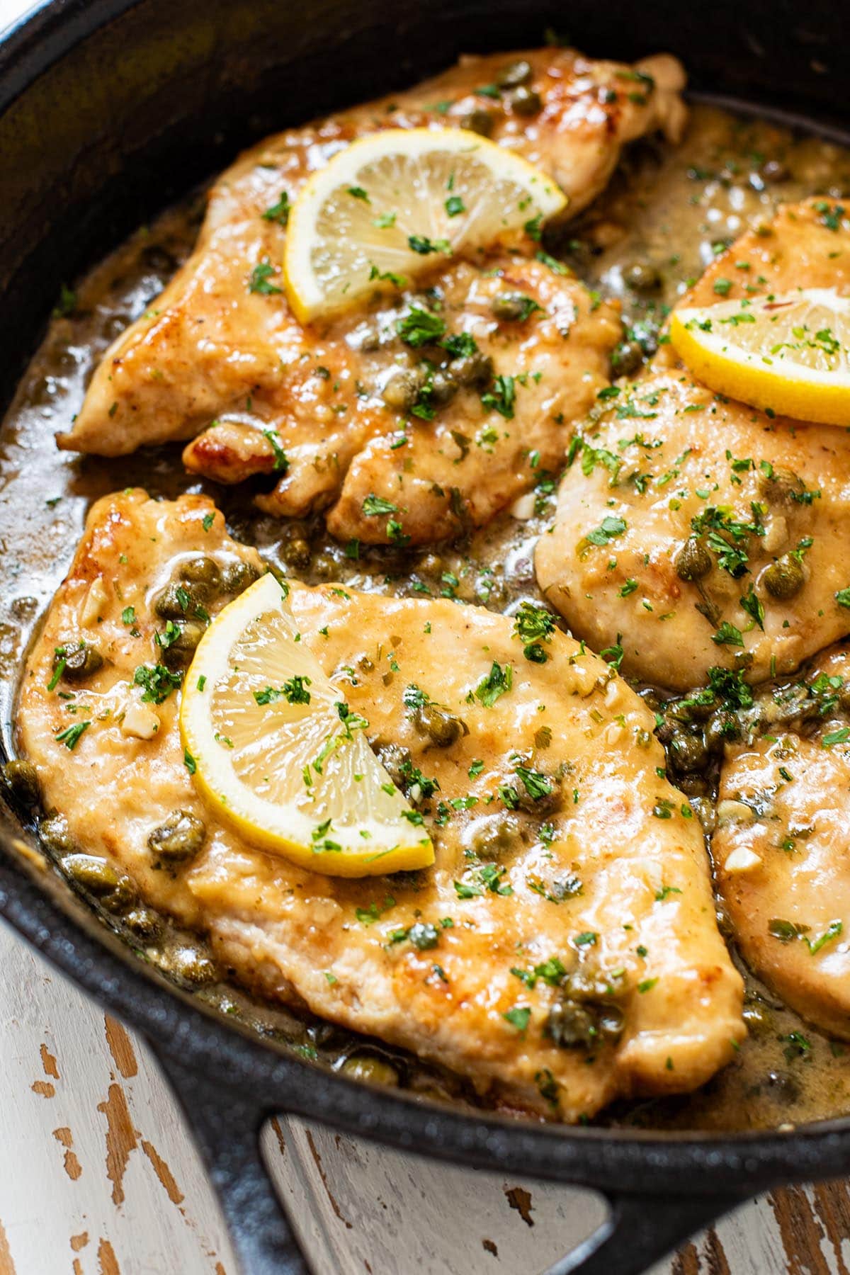 Chicken piccata topped with lemon, capers, and fresh parsley in a cast iron skillet.