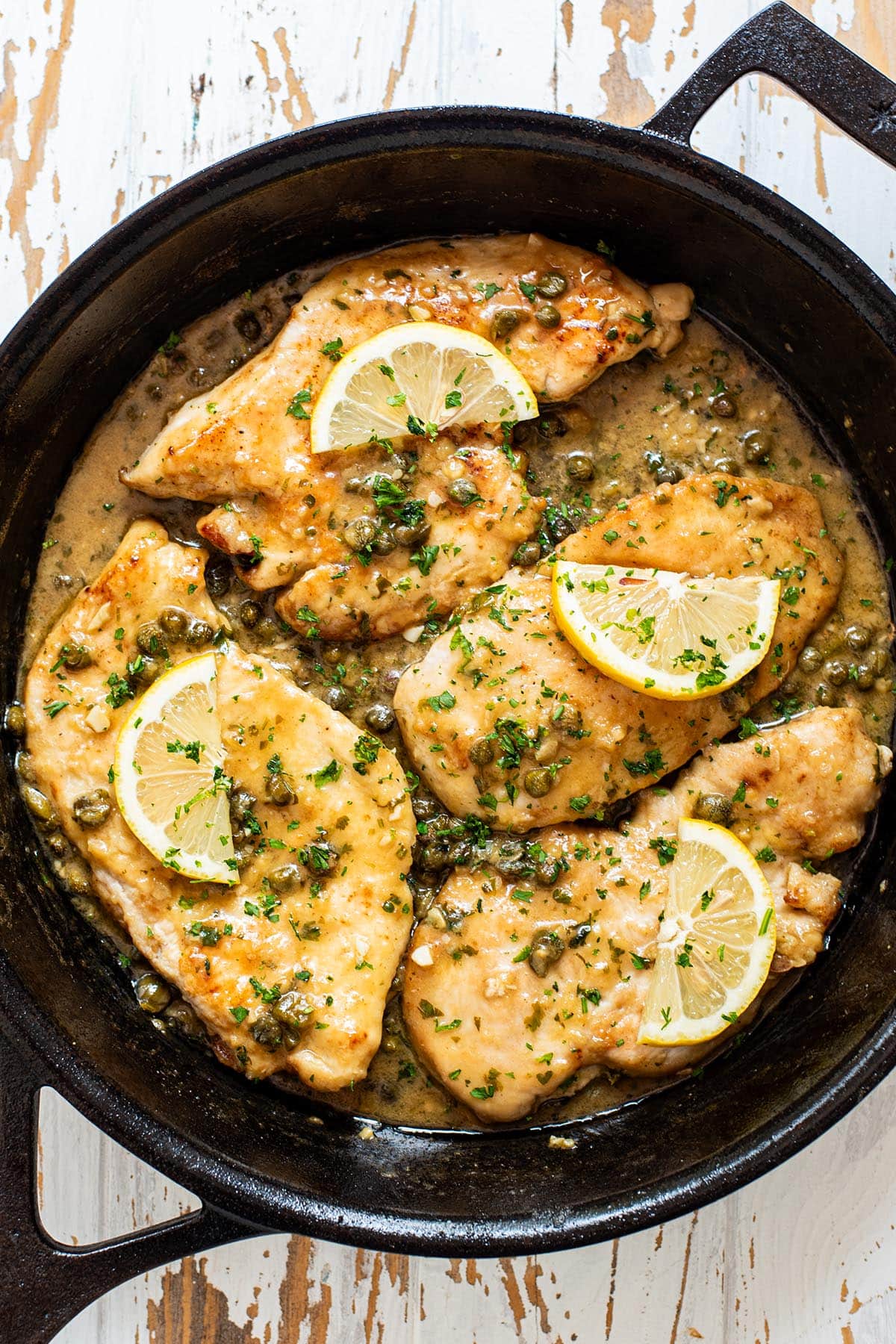 Chicken piccata topped with lemon, capers, and fresh parsley in a cast iron skillet.