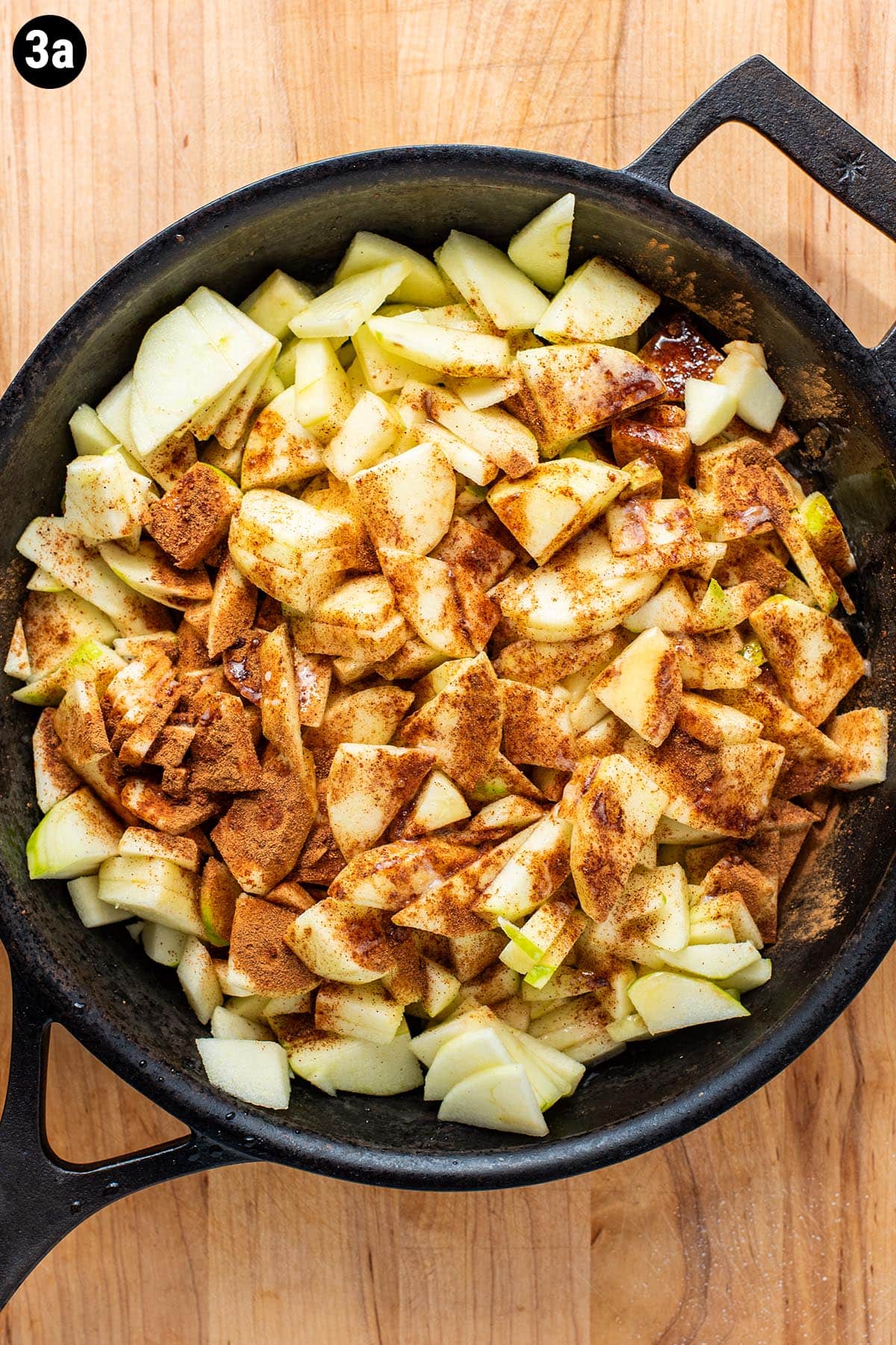 Sliced granny smith apples in a cast iron skillet topped with ground cinnamon, nutmeg, and melted butter.