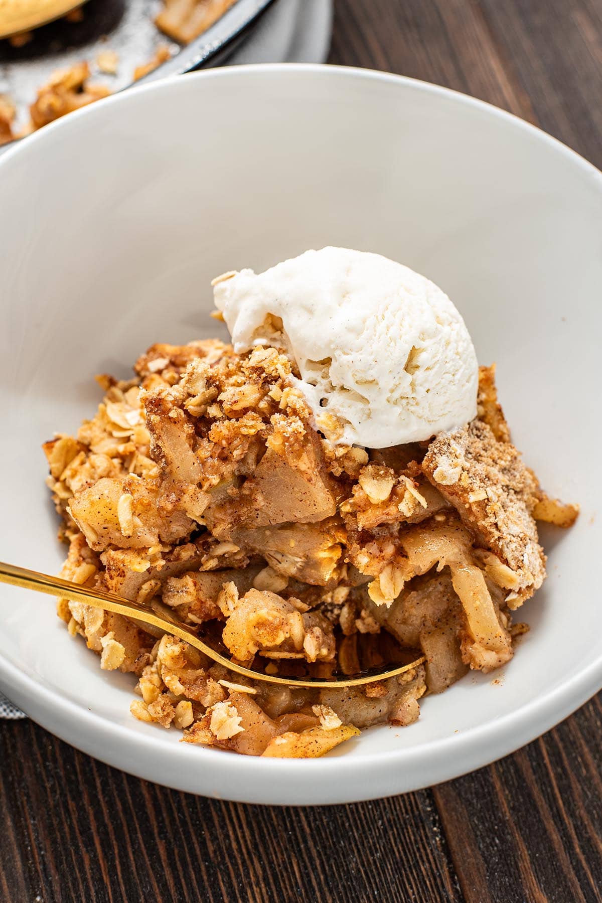 A bowl of golden apple crisp topped with melting vanilla ice cream.