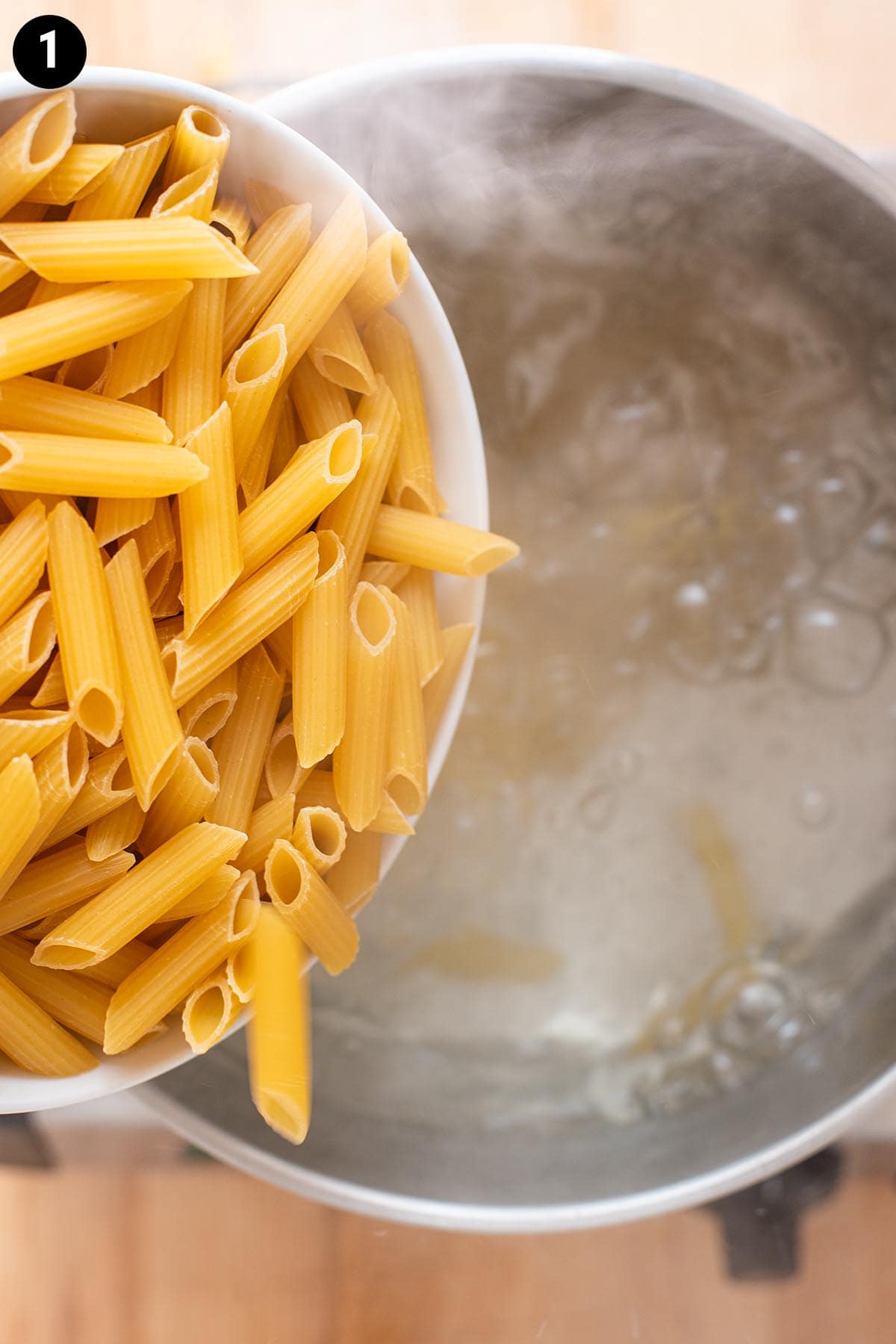 Pouring uncooked penne pasta into boiling water.