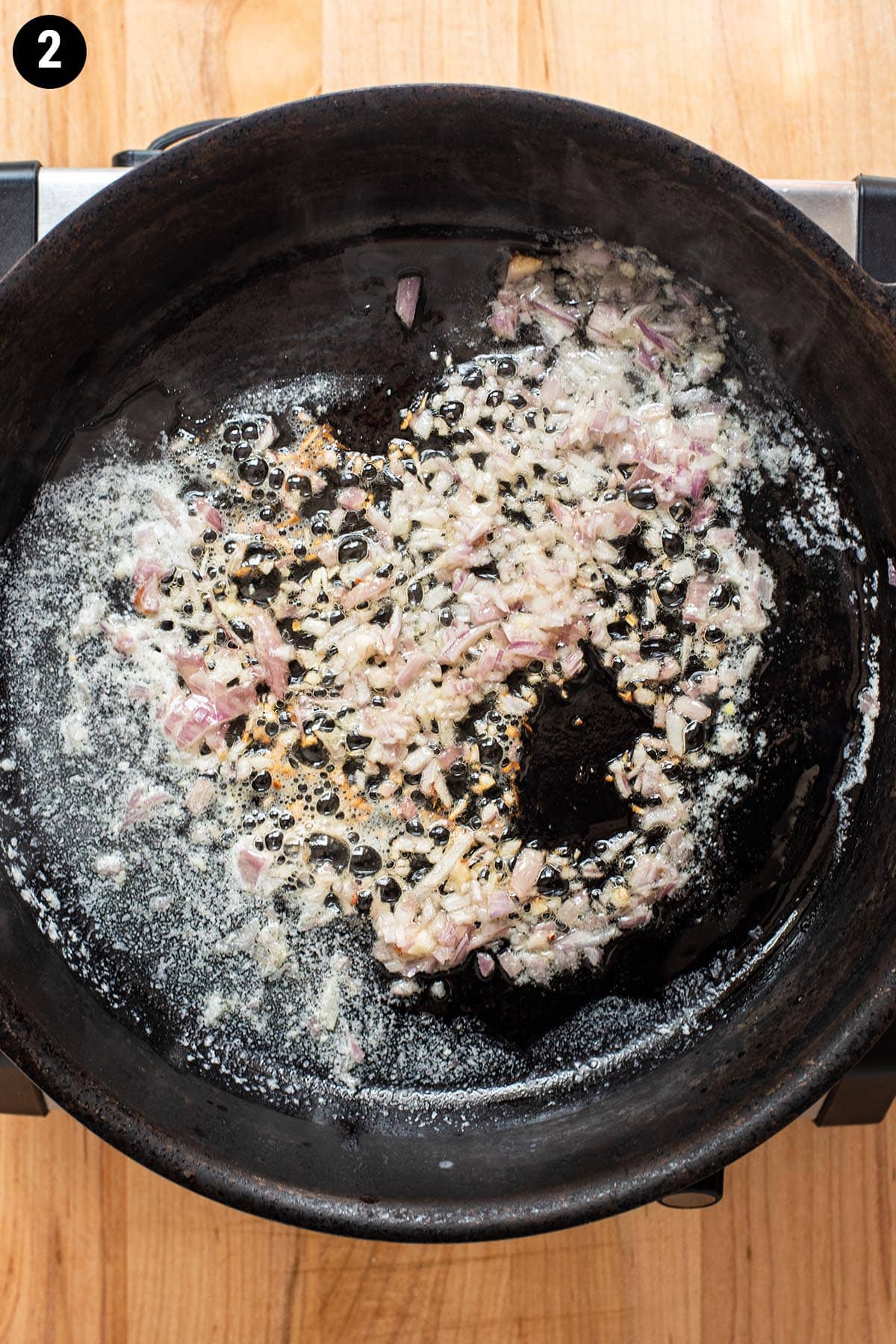 Minced shallots and garlic simmering in a skillet with butter.