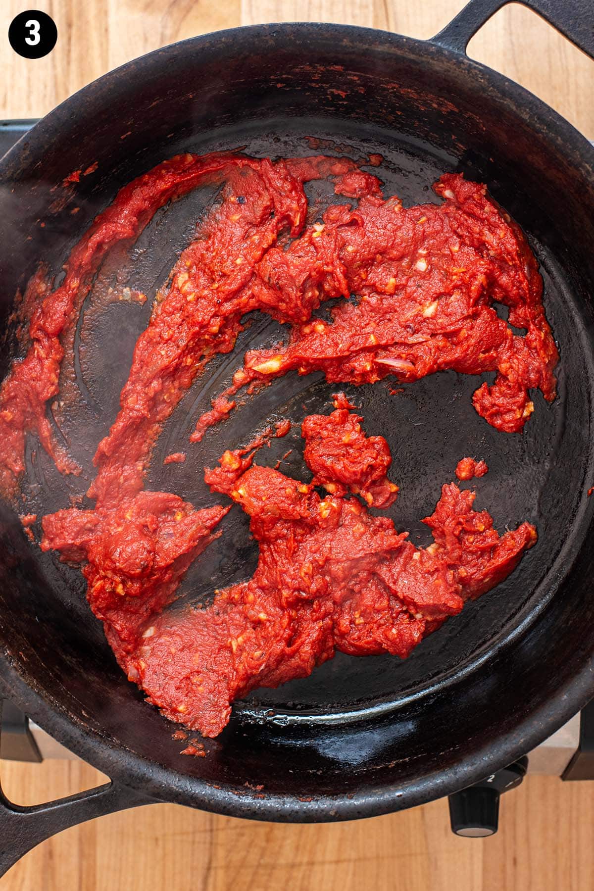 Tomato paste in a hot cast iron skillet with shallot and garlic.