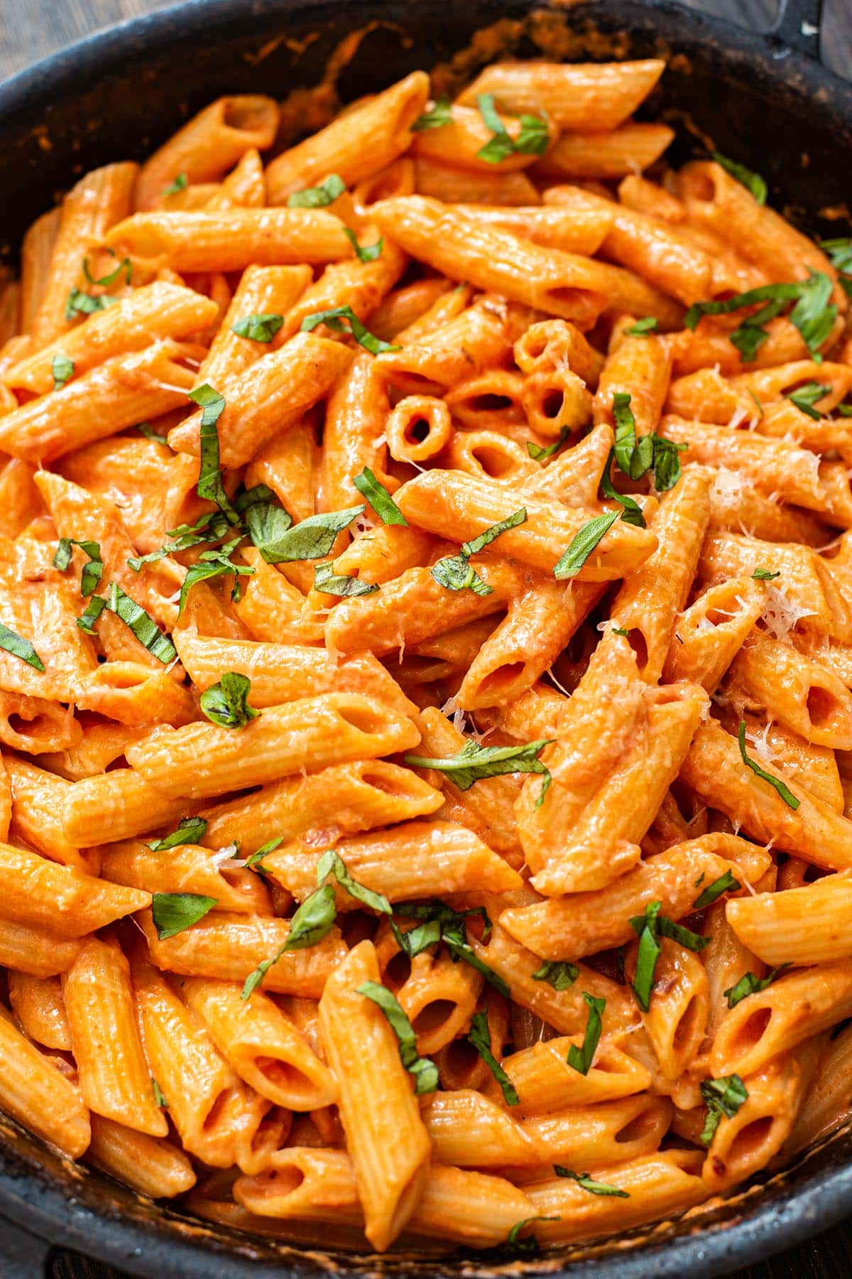 Creamy penne alla vodka in a cast iron skillet topped with fresh basil and freshly grated parmesan cheese.