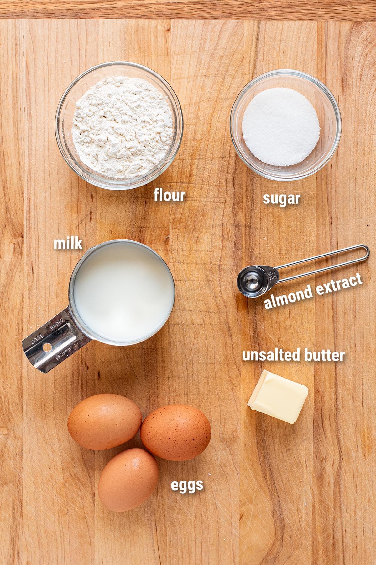 Raw, uncooked Dutch baby ingredients laid out on a wooden cutting board.