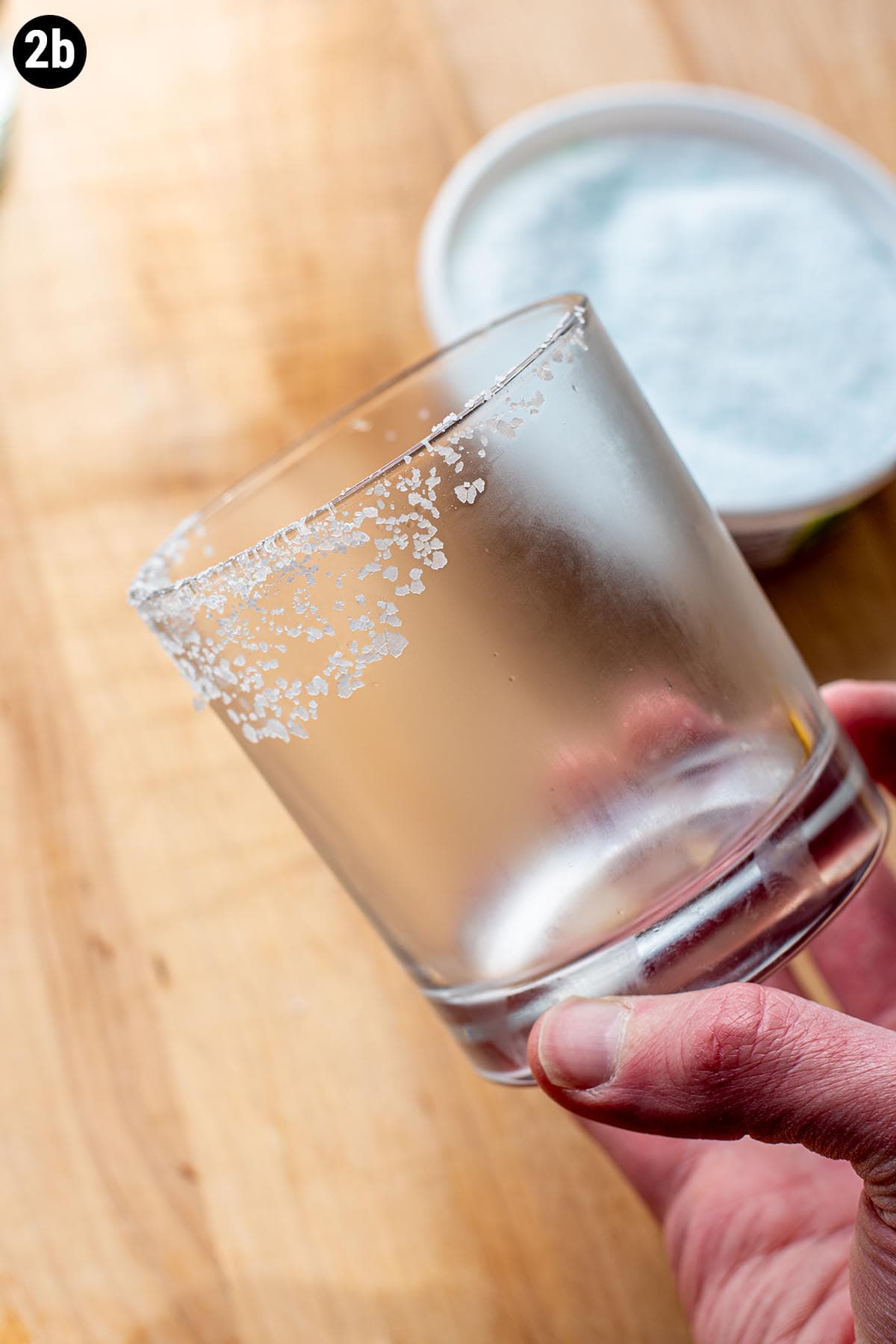 A hand holding an empty chilled glass with a salted rim.