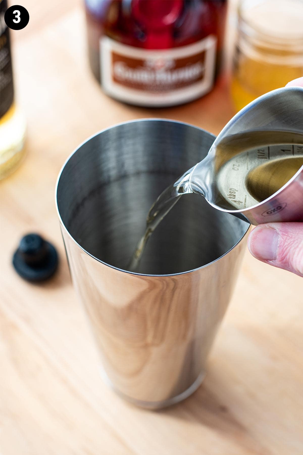 Pouring reposado tequila with a double jigger into a cocktail shaker.