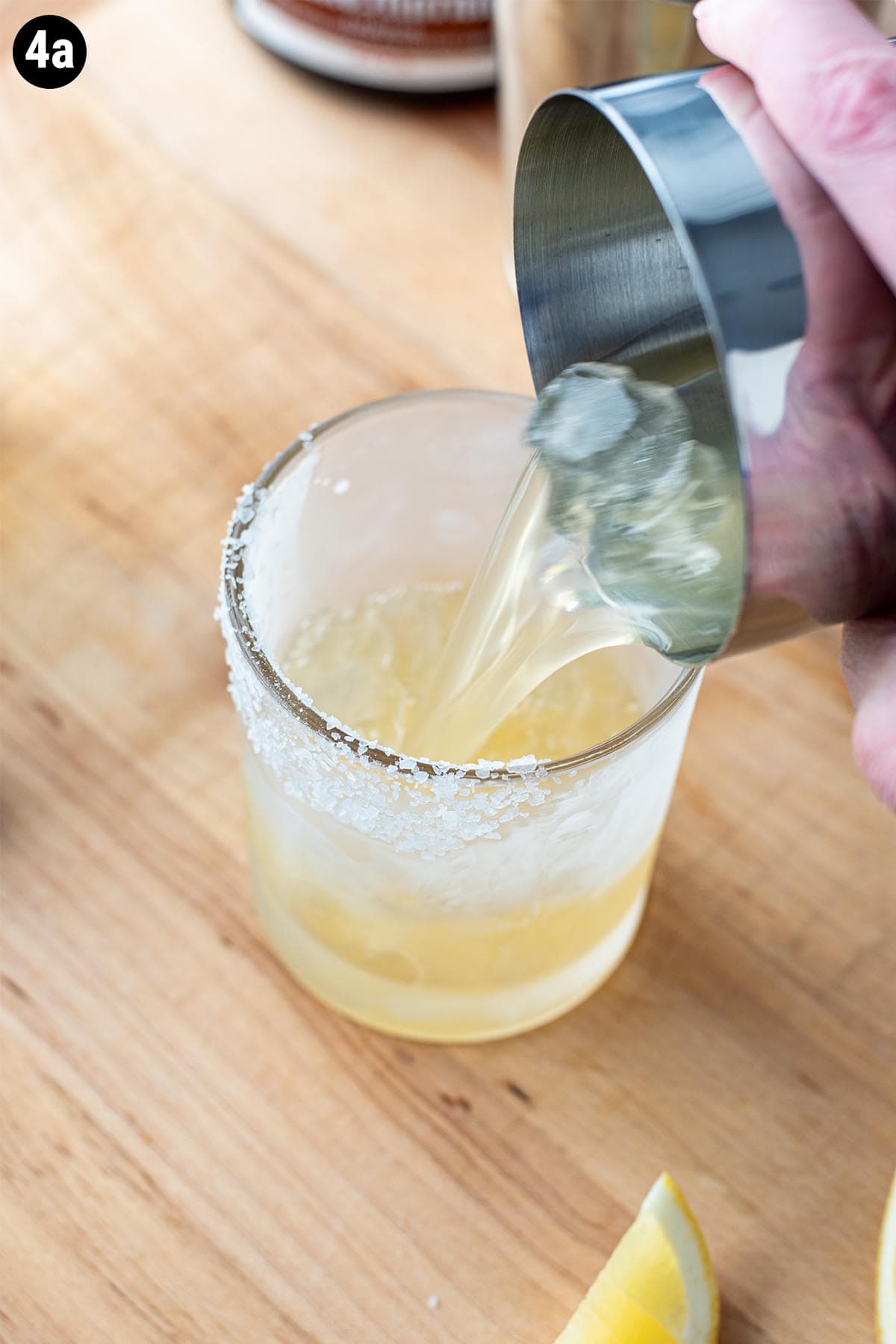 Pouring a margarita from a cocktail shaker into a chilled glass with a salted rim.