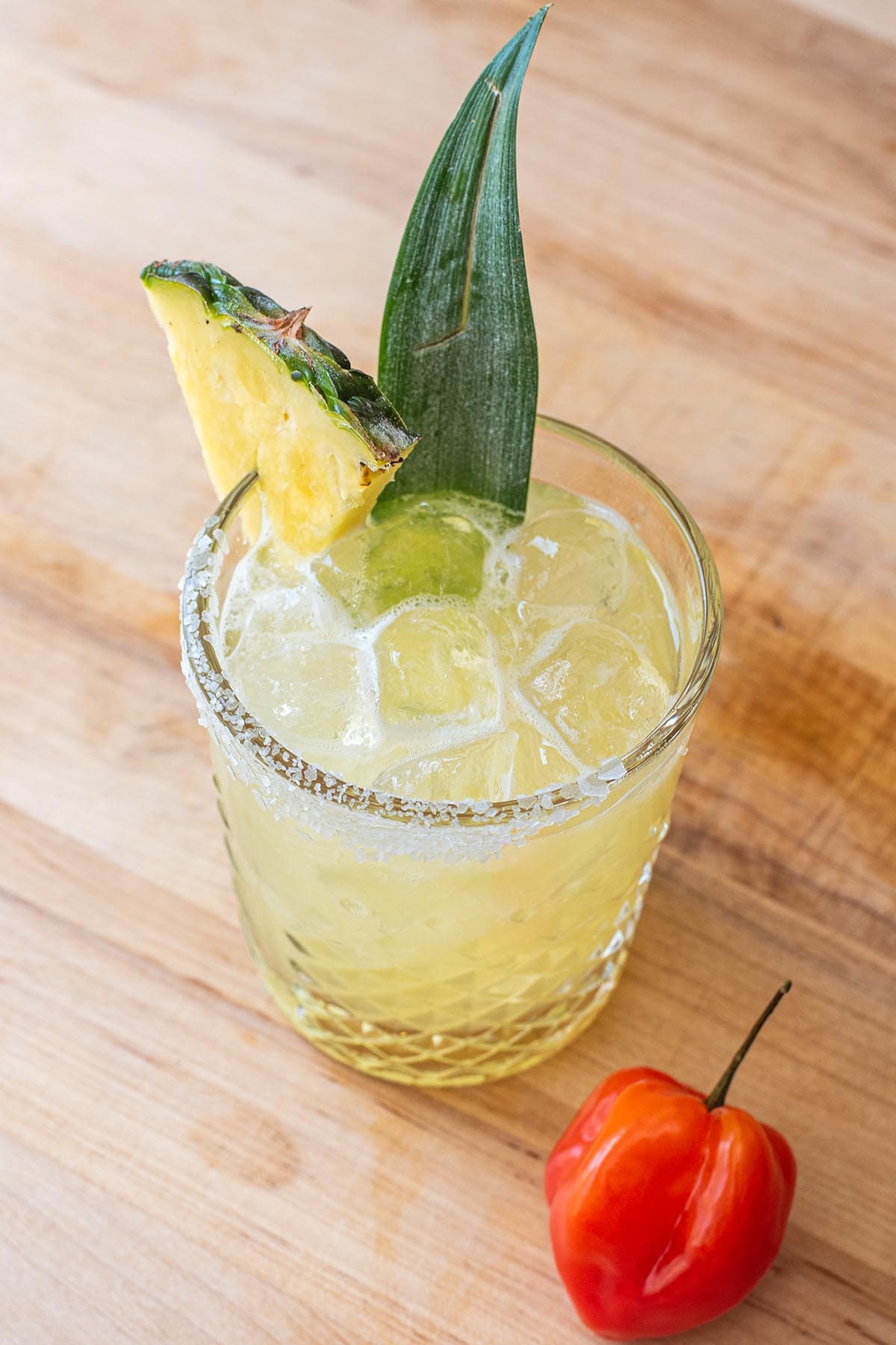 A pineapple habanero margarita pictured in a glass with a salted rim and garnished with a pineapple wedge.