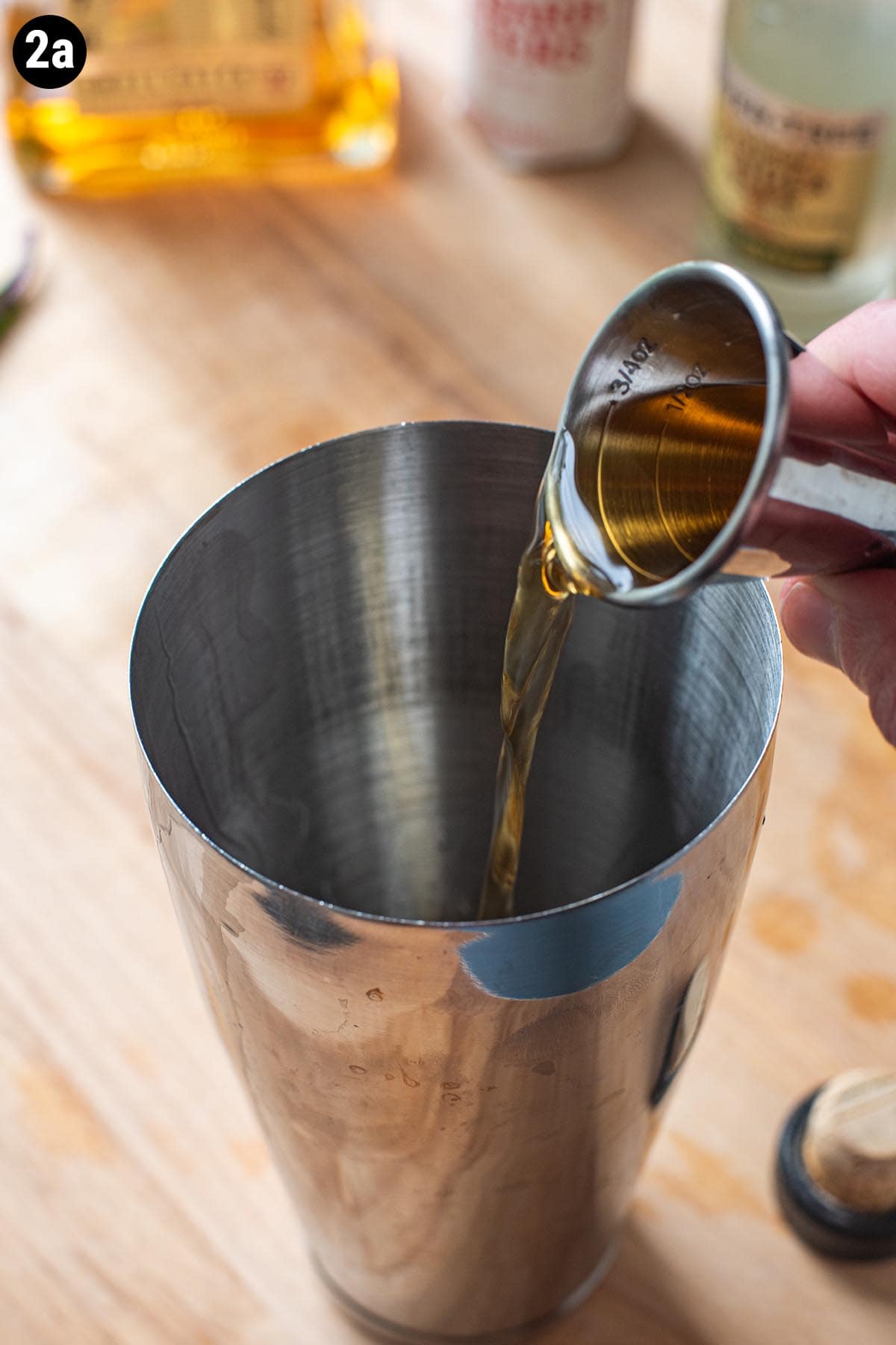 A hand pouring a double jogger of bourbon into a cocktail shaker.