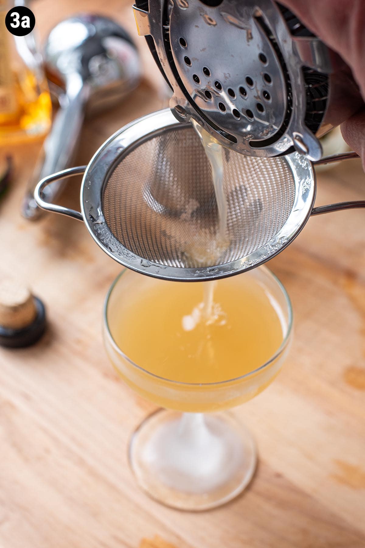 Double straining a golden bourbon based cocktail into a chilled coupe glass.