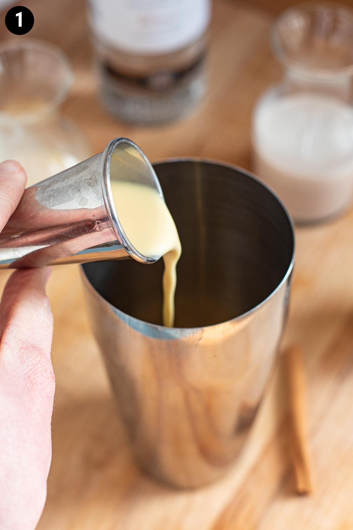 Pouring eggnog into a cocktail shaker with a cocktail jigger.