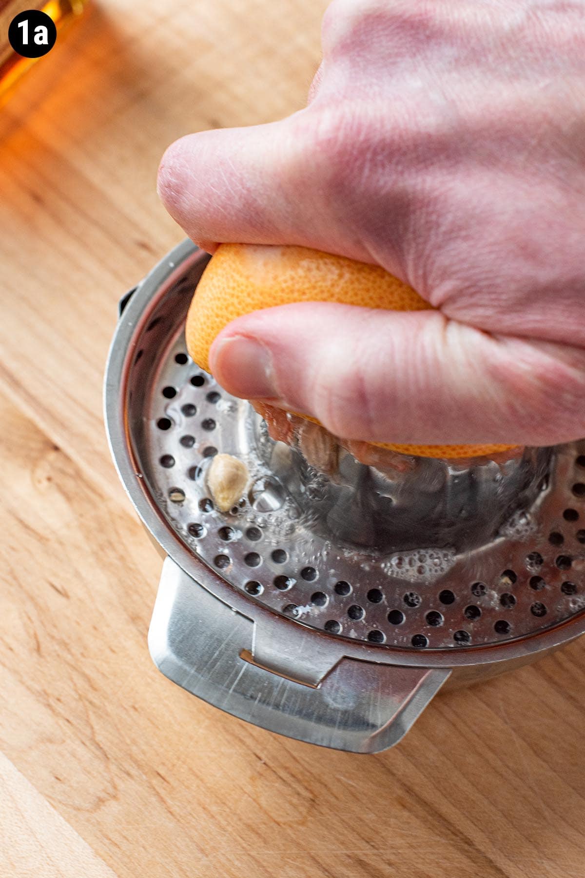 A hand using a handheld citrus juicer to juice a grapefruit.