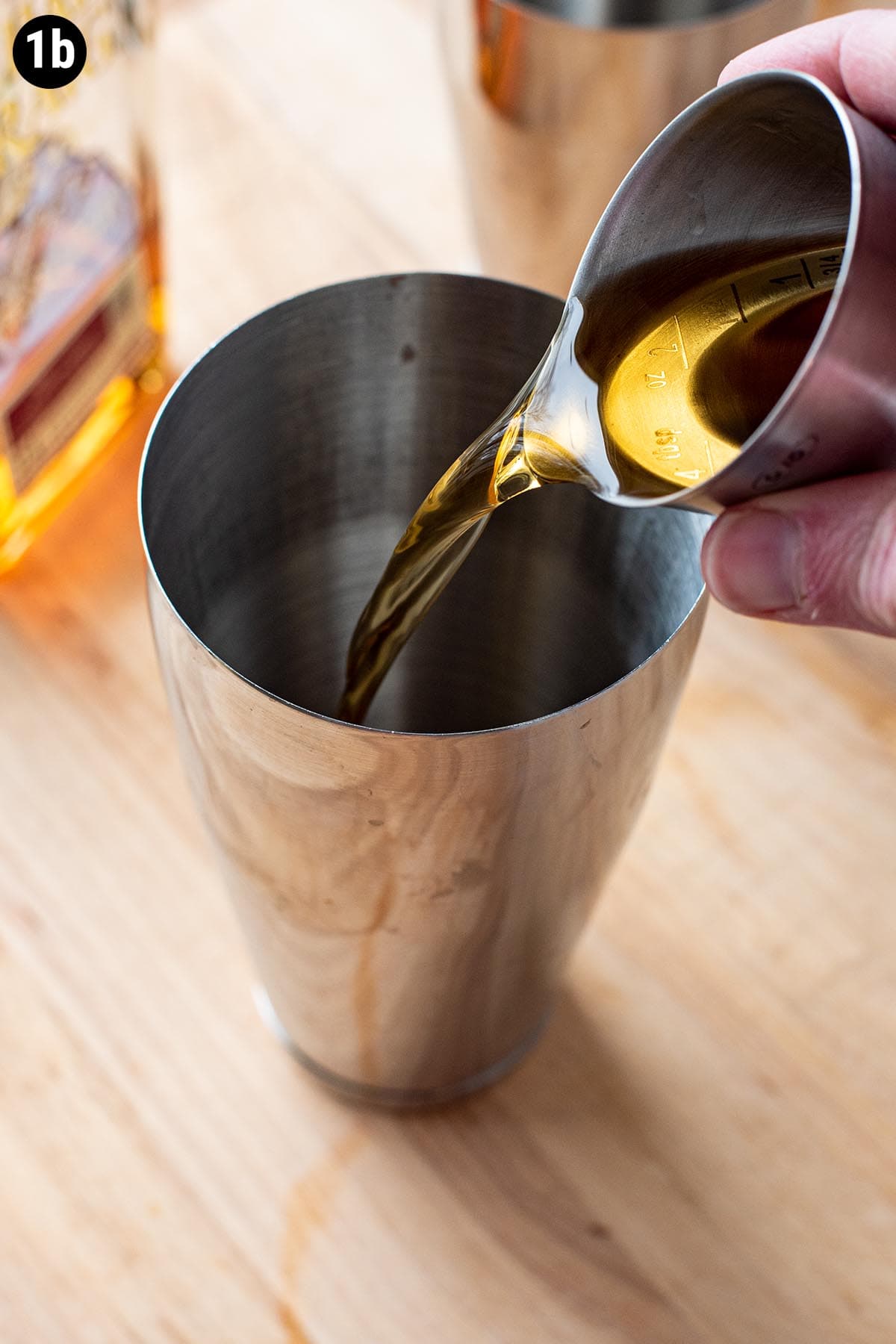 Pouring bourbon into a cocktail shaker with a 2 ounce jigger.