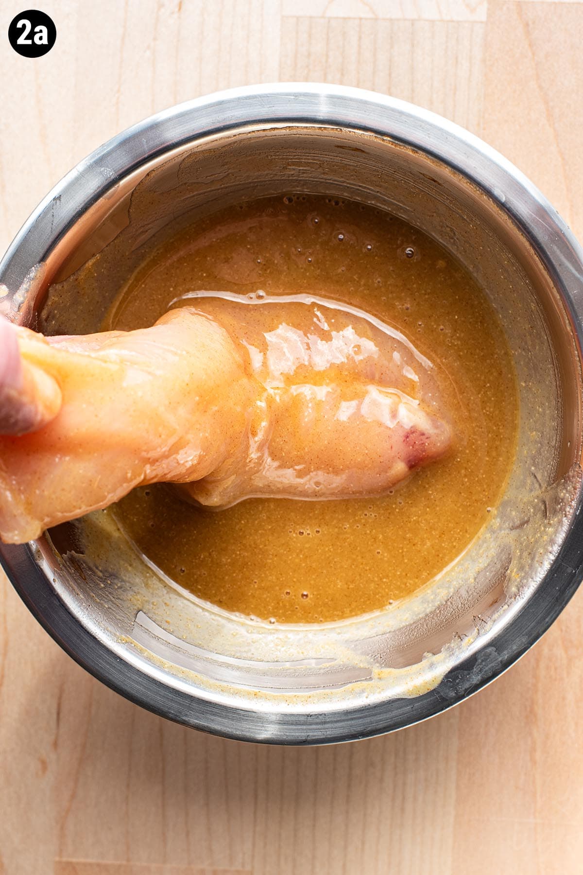 Dredging a raw, unbreaded chicken tender in honey-Dijon mustard.
