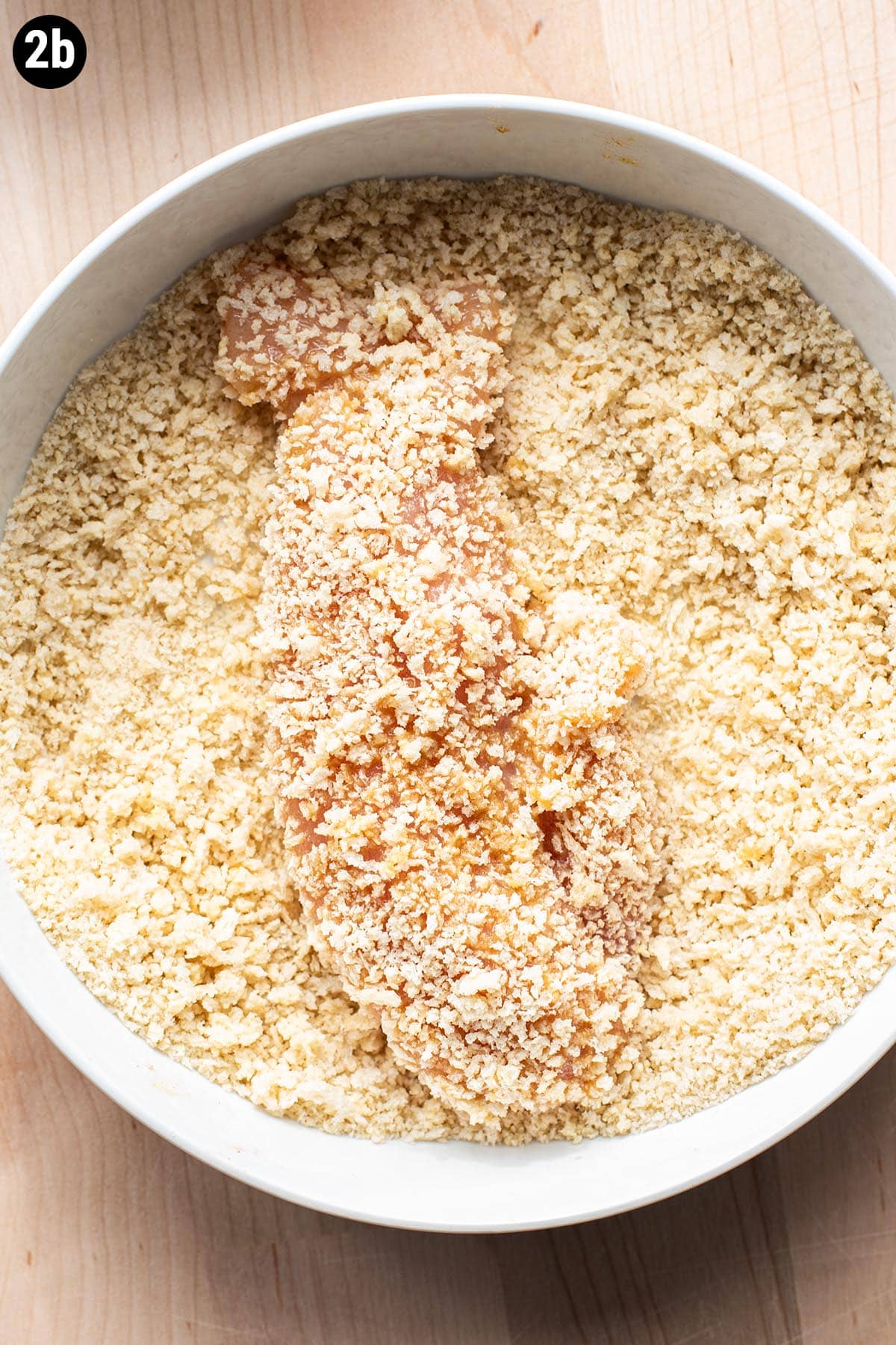 Dredging a chicken tender in panko crumbs in a shallow dish.