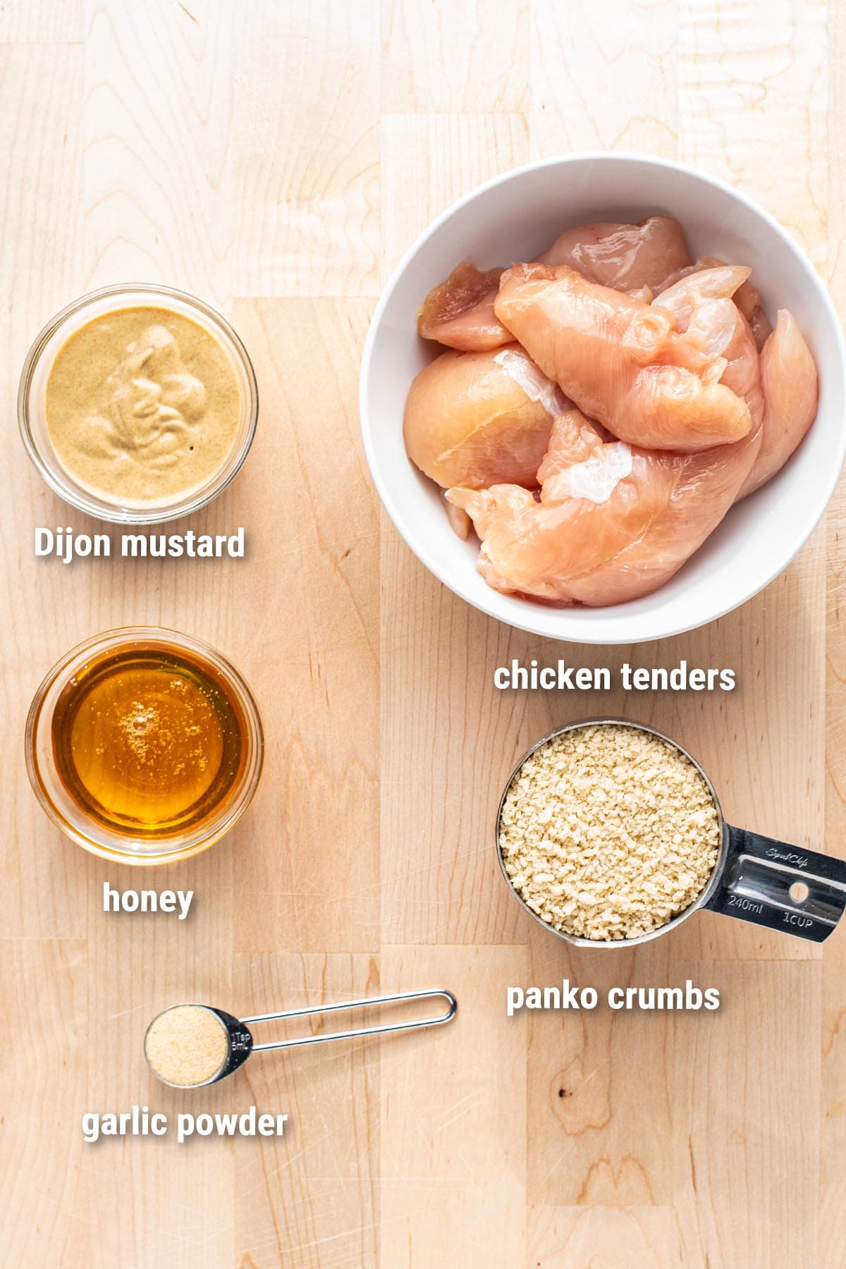 Raw, uncooked baked honey mustard  chicken tenders ingredients arranged on a wooden cutting board.